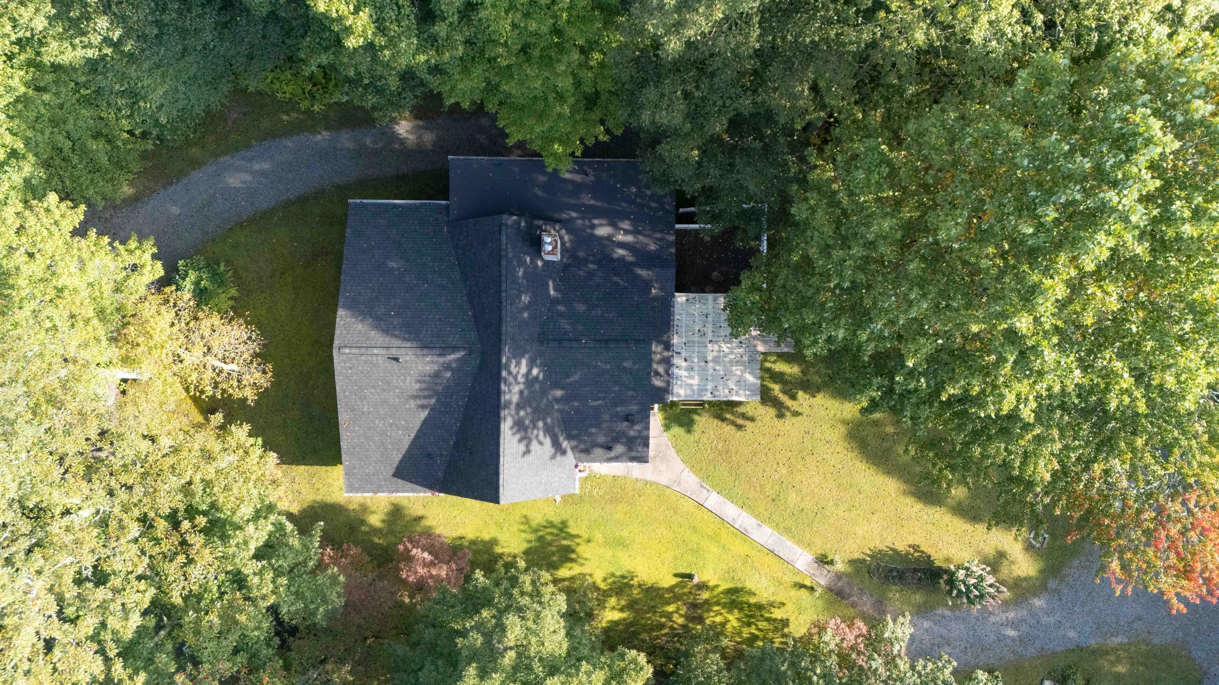 An aerial view of a house surrounded by green trees and a curved driveway with a grassy yard.