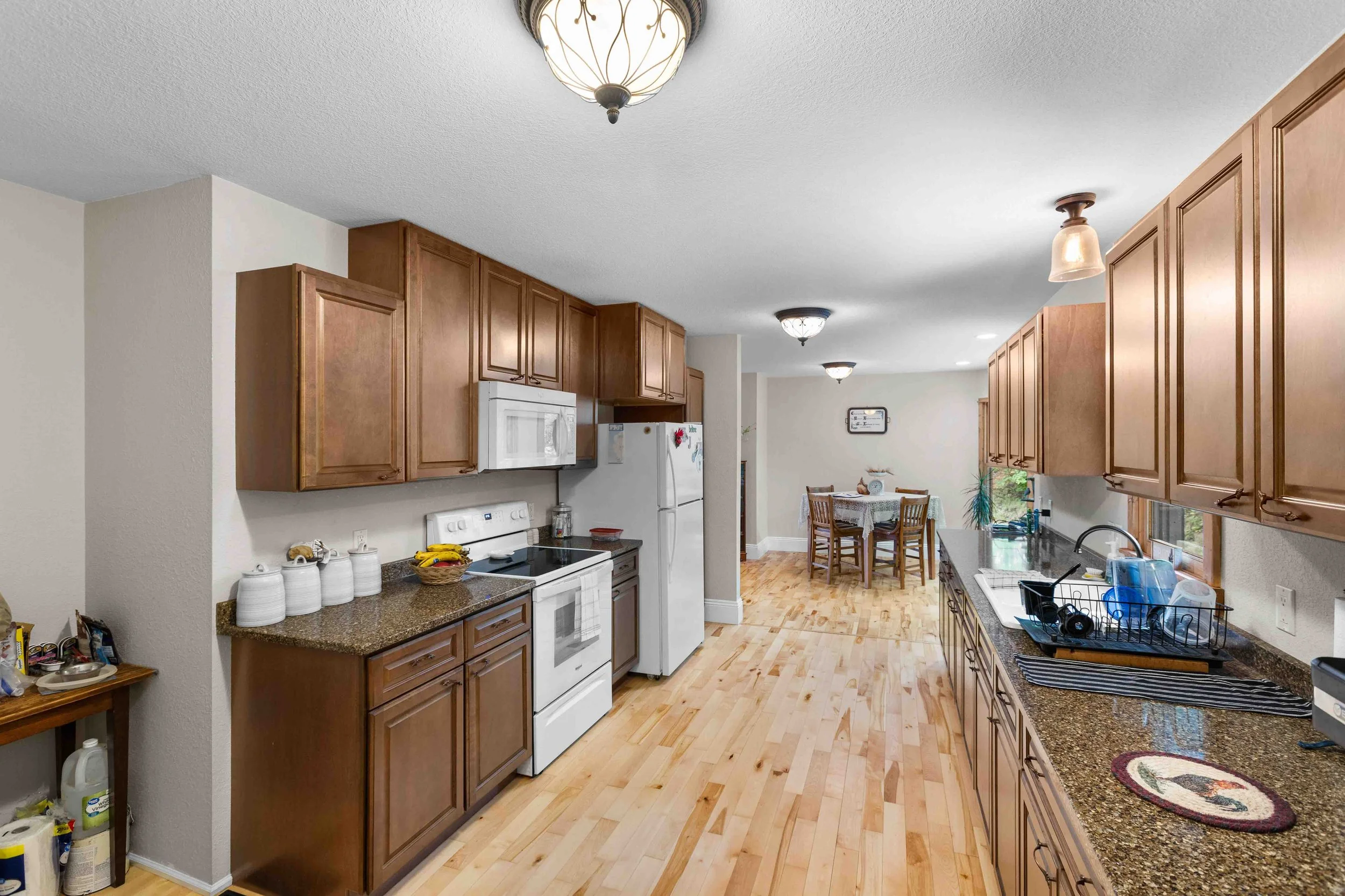 Spacious kitchen with wooden cabinets, white appliances, and a dining area in the background.