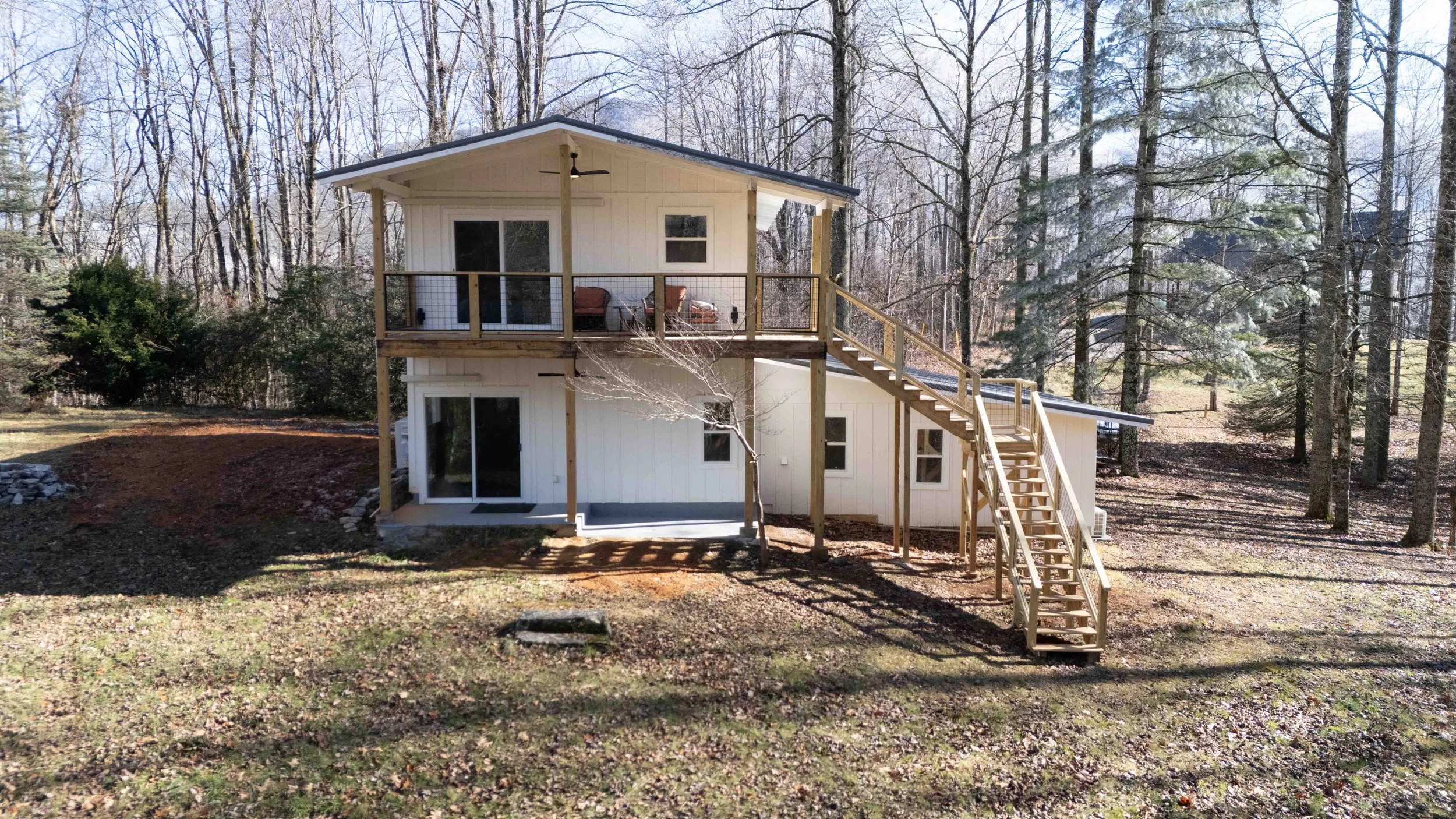 Two-story house with a large deck and stairs leading down to backyard, surrounded by leafless trees.
