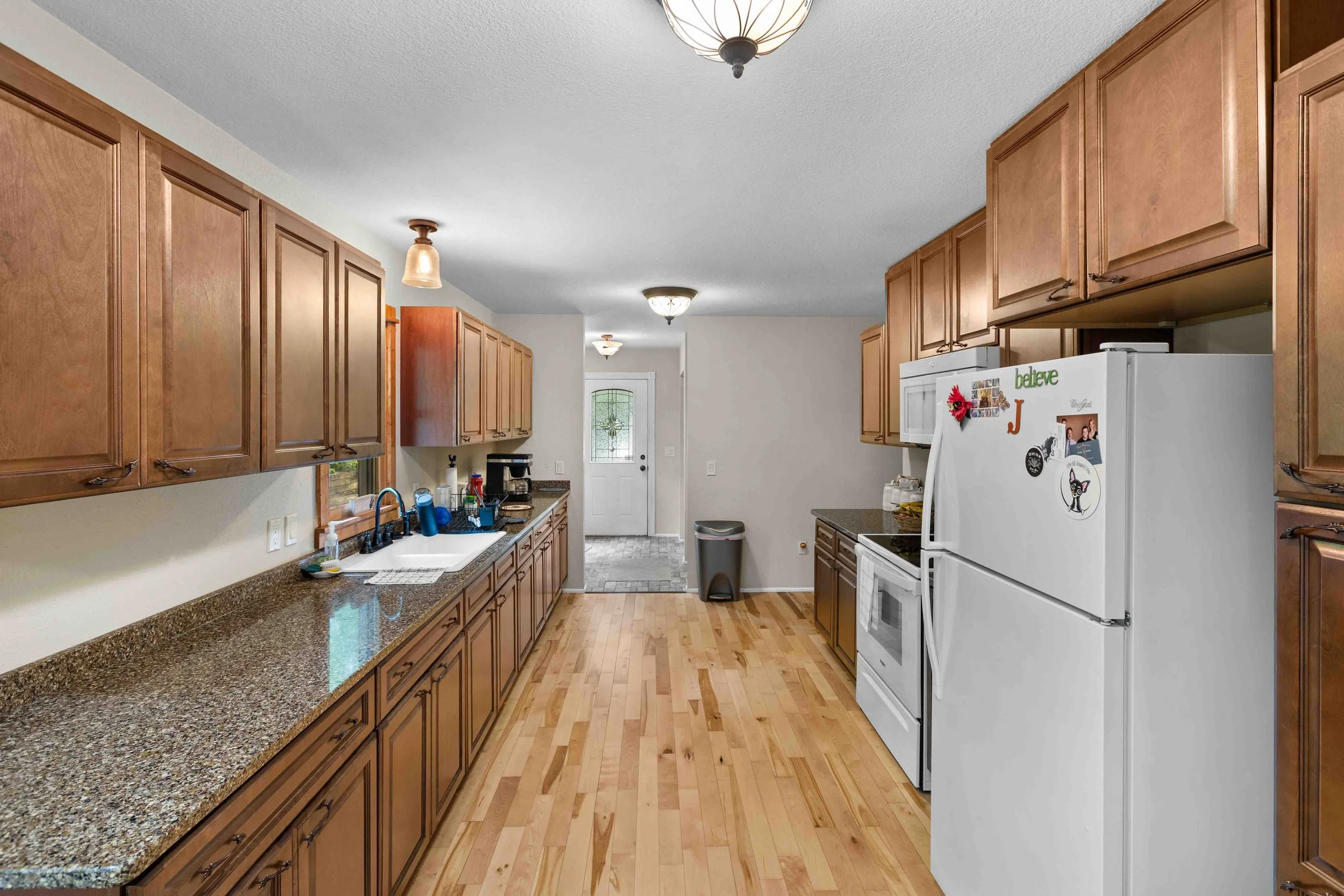 Kitchen with wooden cabinets, granite countertops, white appliances, and hardwood floors, leading to a front door.