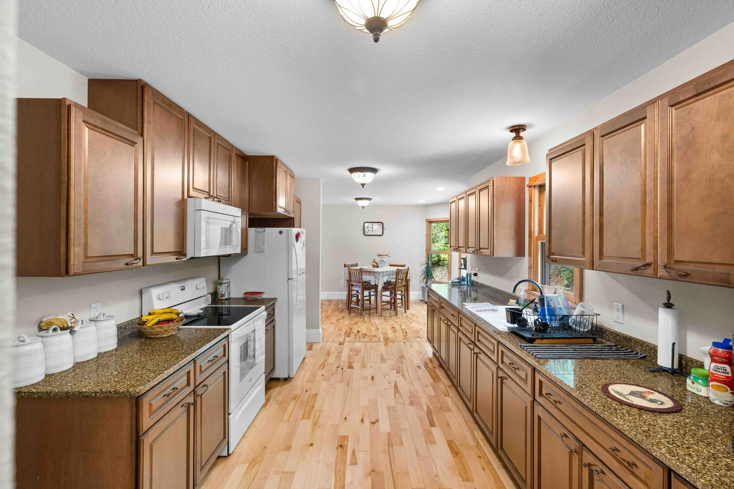 A spacious kitchen with wooden cabinets, white appliances, granite countertops, and a small dining area with a table and four chairs near a window.