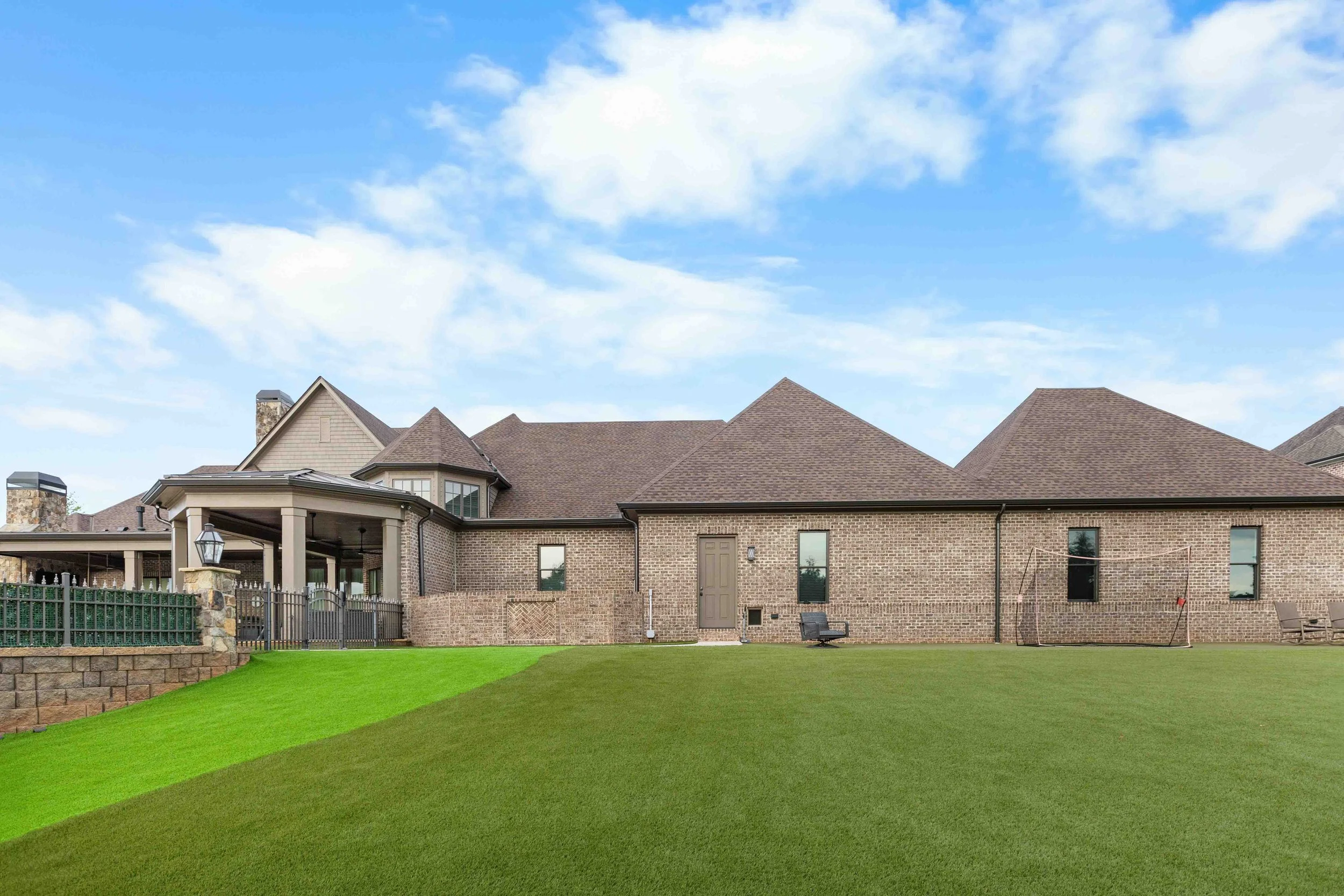 Back of a large brick house with a green lawn and a blue sky with clouds