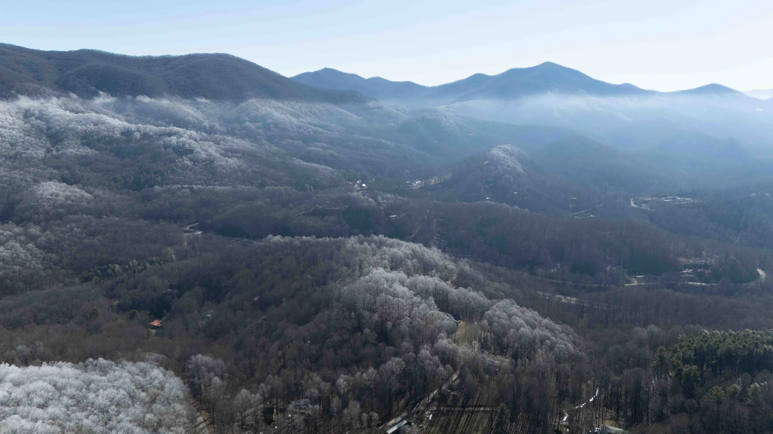 Aerial view of a mountainous landscape with trees and fog in the valleys on a clear day.