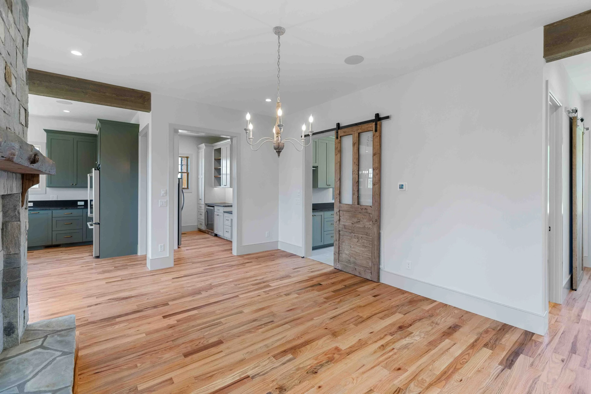 Open-concept living space with hardwood floors, a stone fireplace, a chandelier, and visible kitchen and laundry areas with green and white cabinetry.