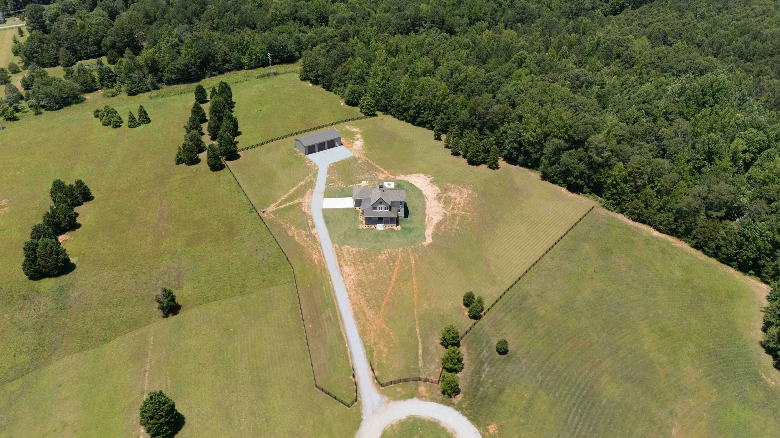 Aerial view of a rural property showing a house with a circular driveway, a gravel road leading to a detached garage, surrounded by green fields and trees.
