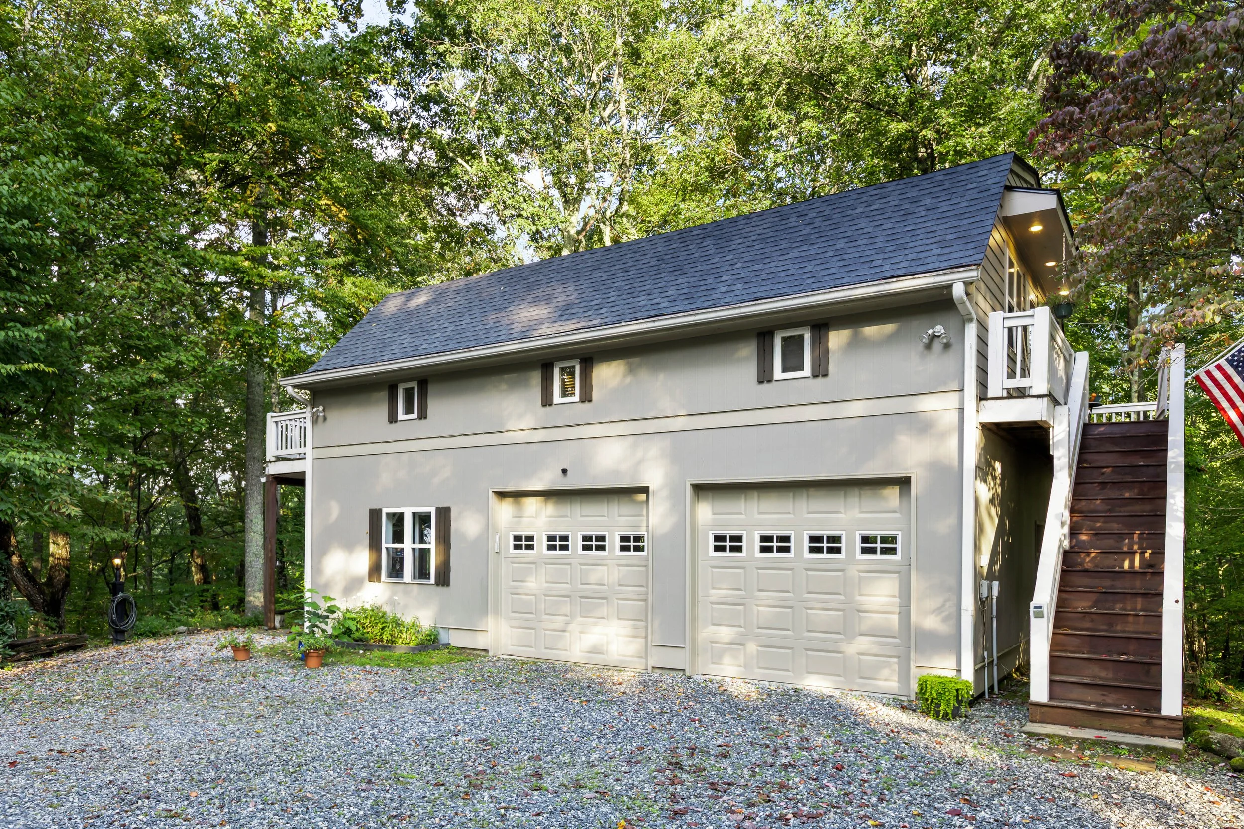 A two-story house with a garage, surrounded by trees and a gravel driveway.