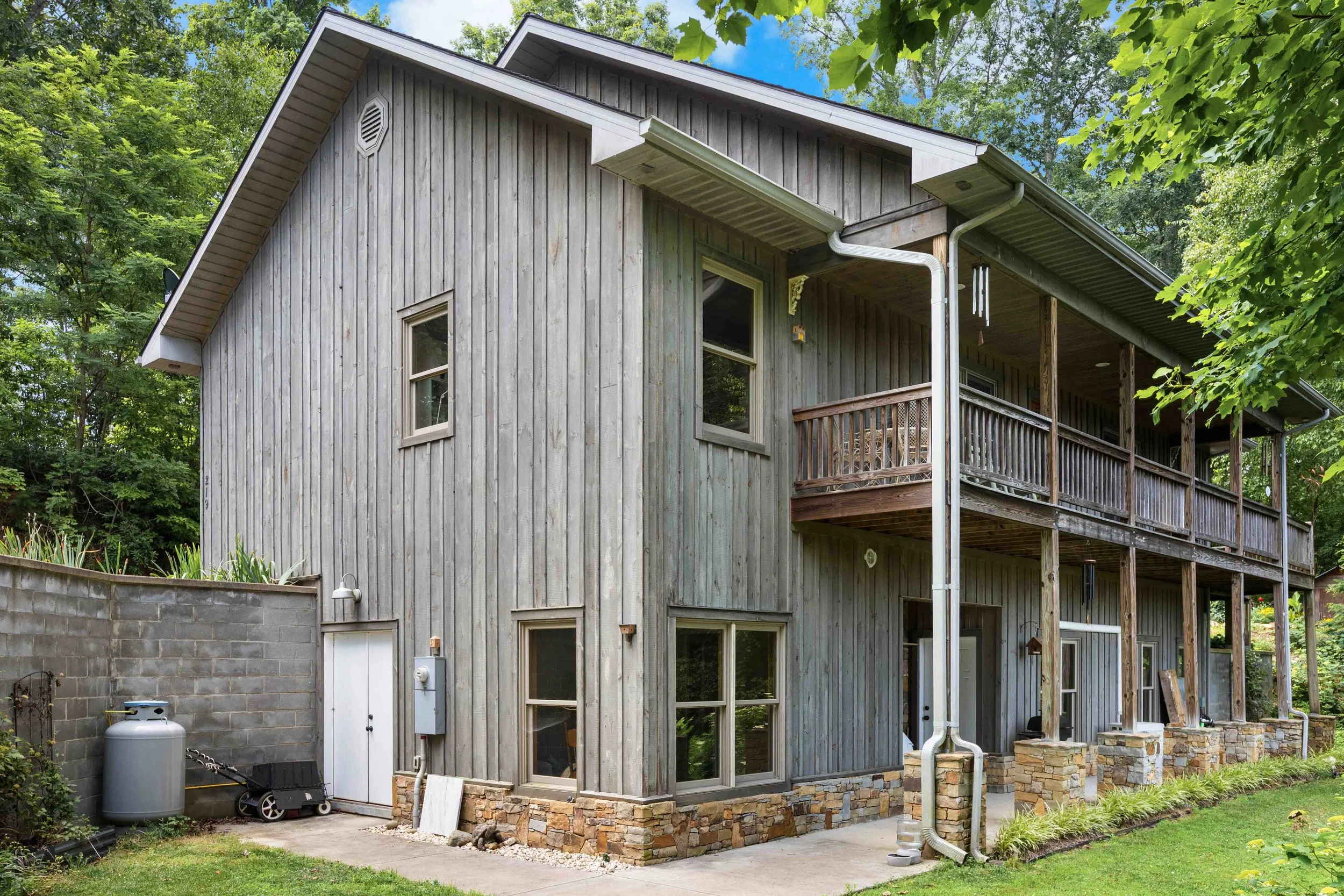 Rear view of a two-story wooden house with a balcony, surrounded by greenery.