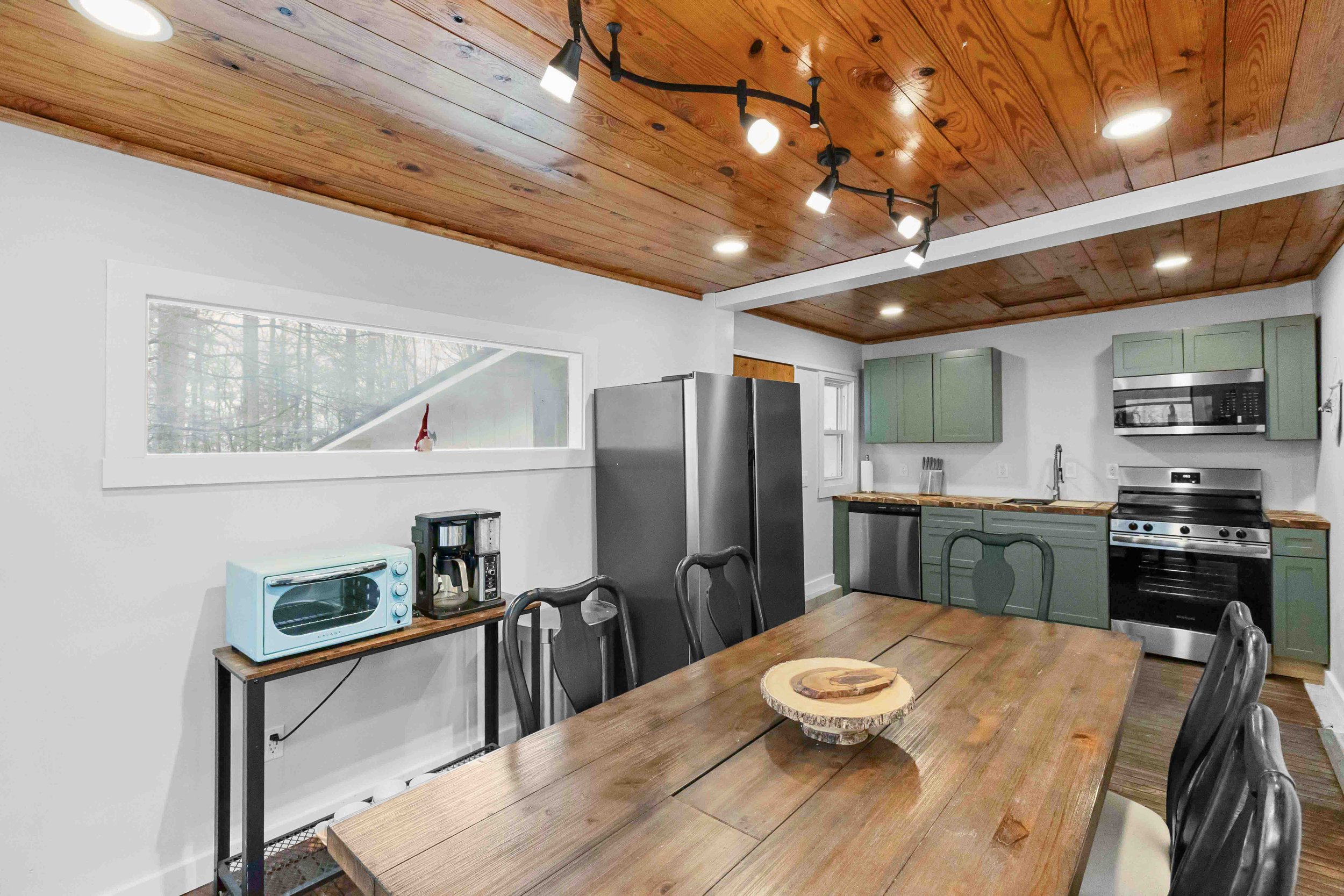 Kitchen with wooden ceiling, green cabinets, stainless steel appliances, and a wooden dining table with six black chairs.