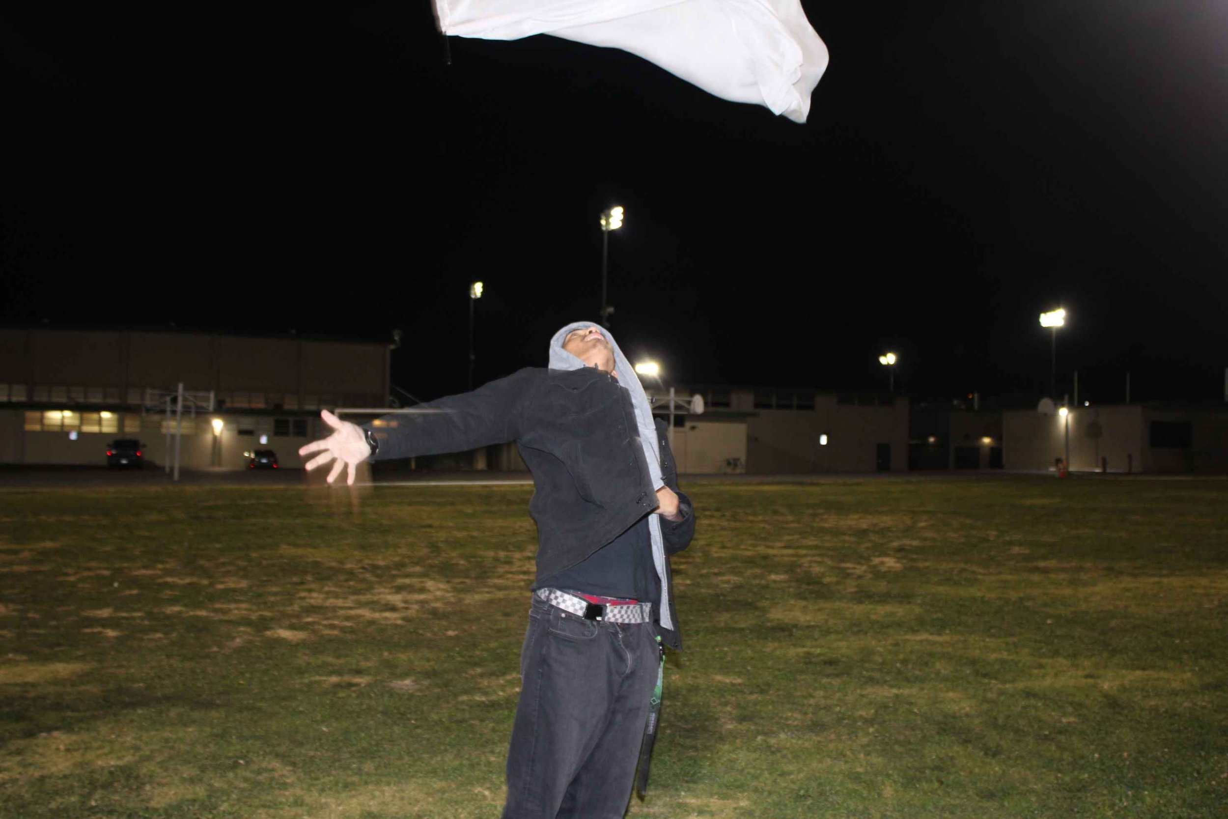 Person tossing a cloth in the air on a grassy field at night