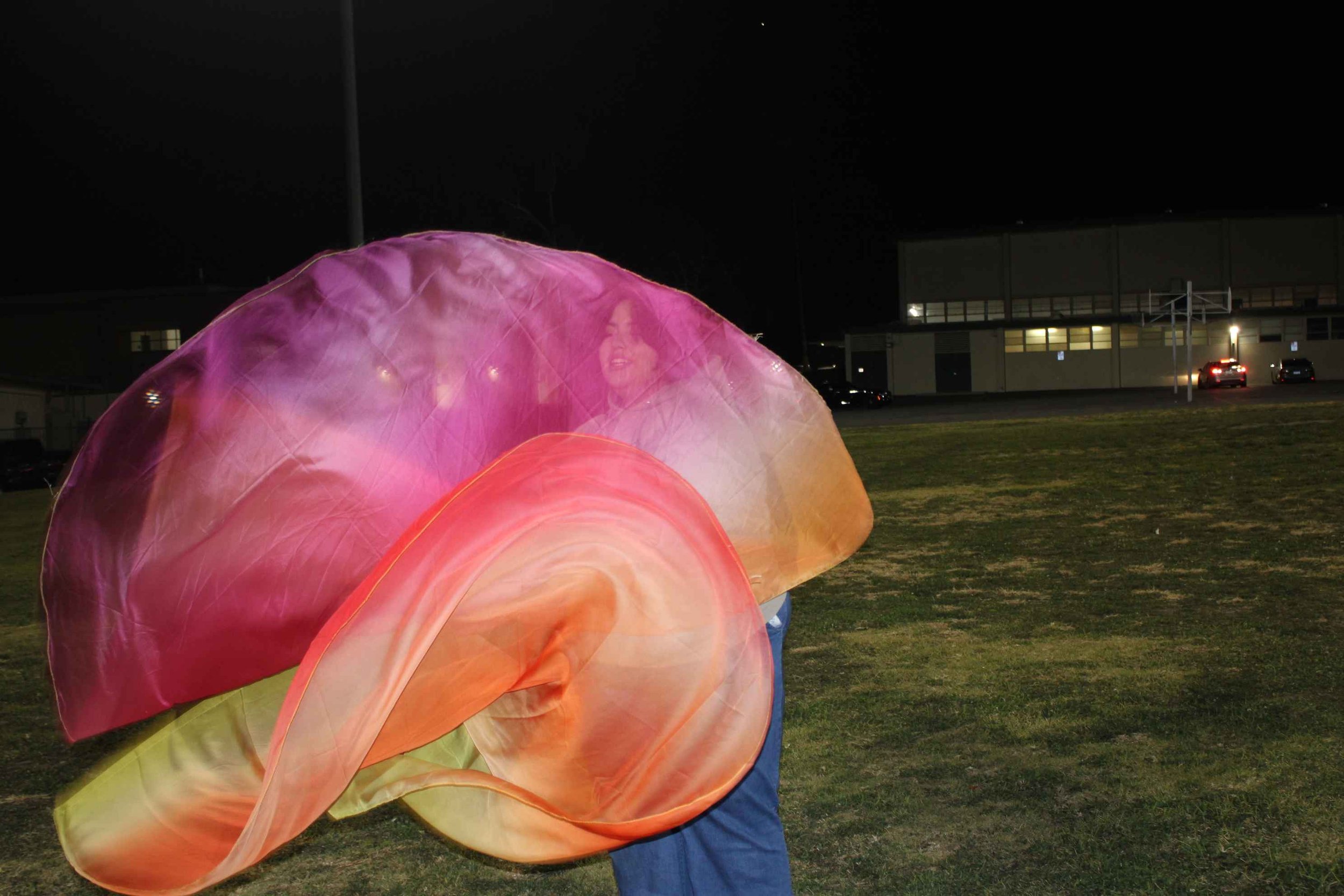 Person outdoors at night dancing with colorful, flowing fabric.