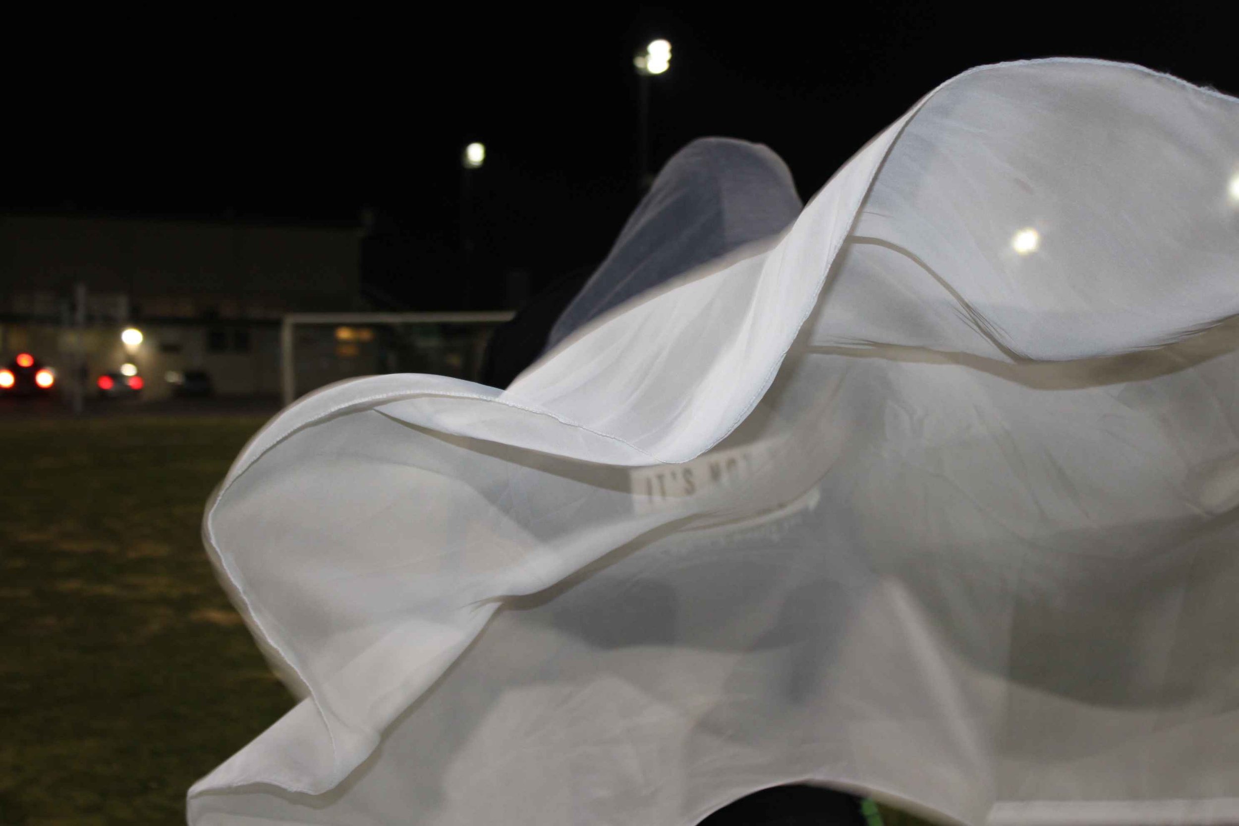 Close-up of a white fabric blowing at night with blurred background lights.