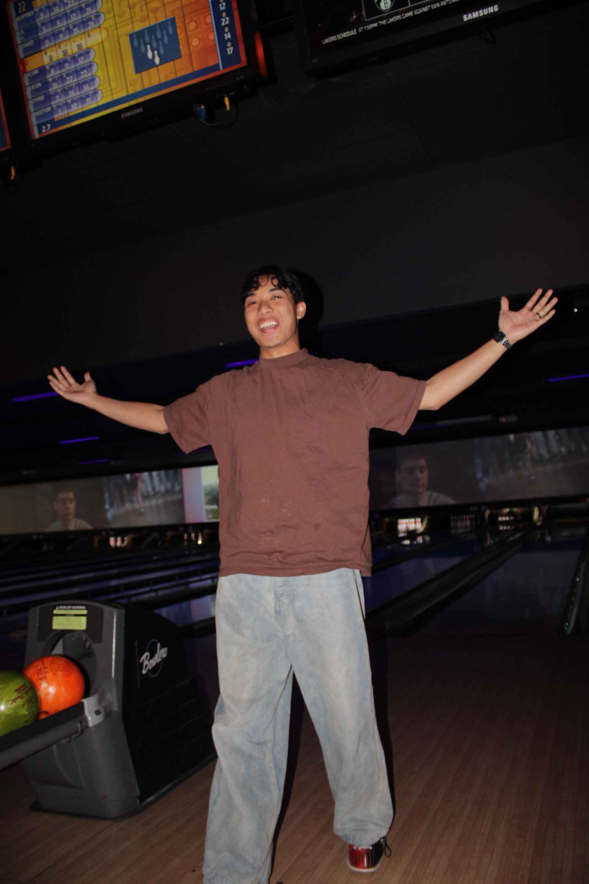 Person celebrating in bowling alley with arms raised, wearing casual clothes.