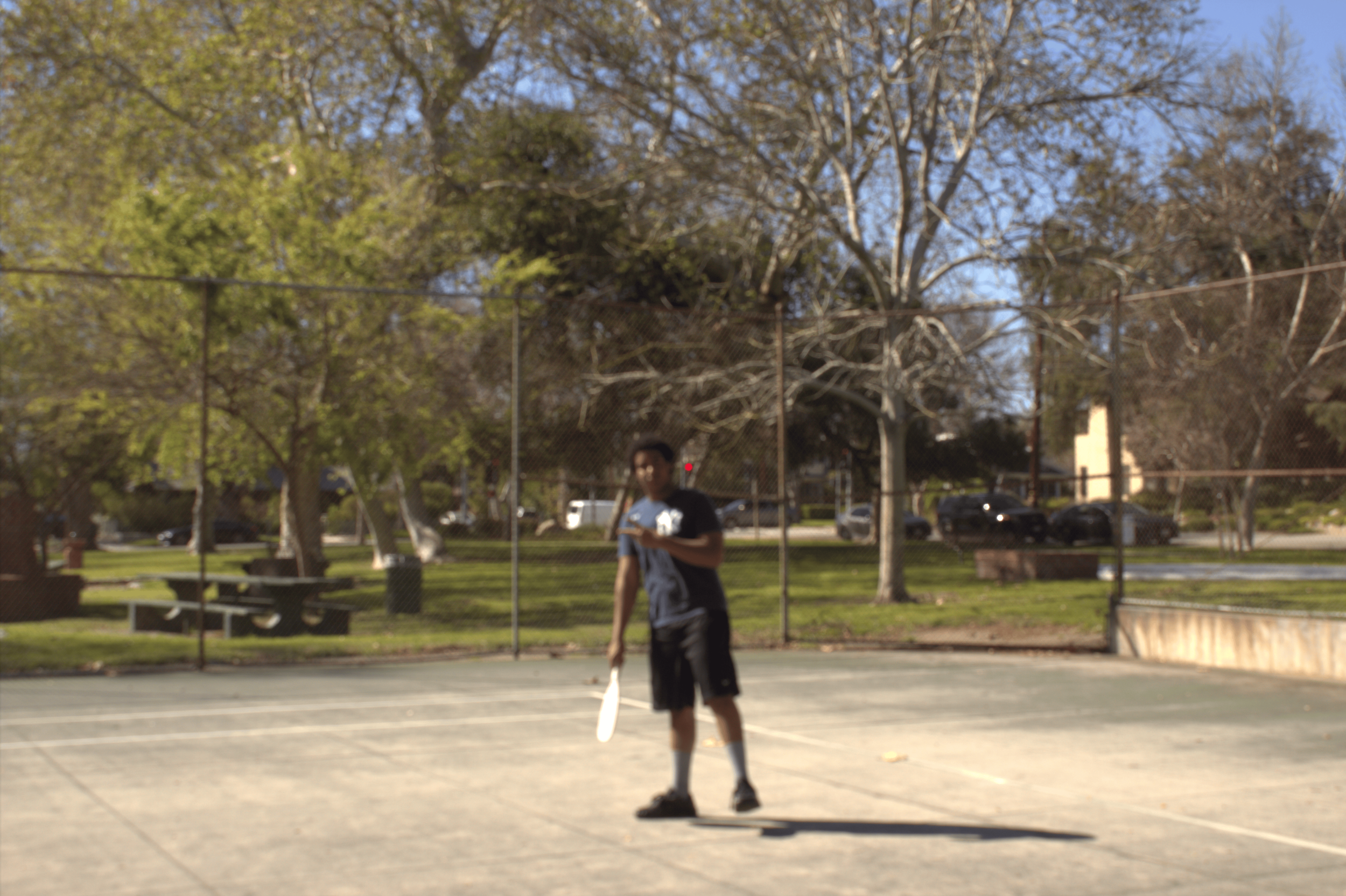 Person playing tennis on an outdoor court in a park