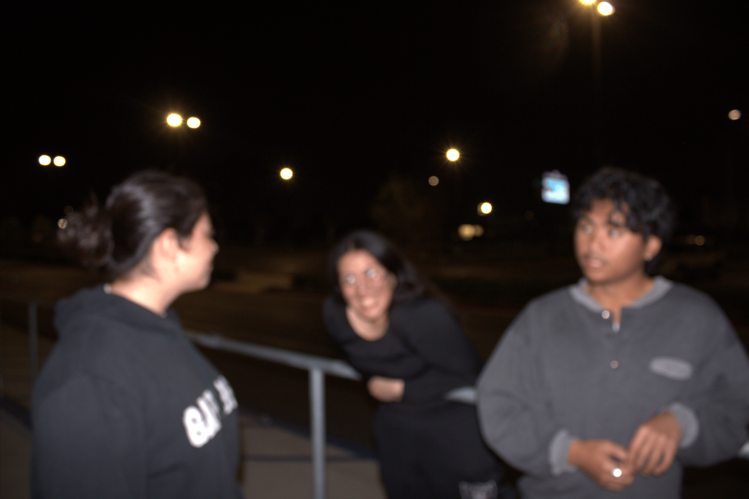 Blurry image of three people outdoors at night with streetlights in the background.
