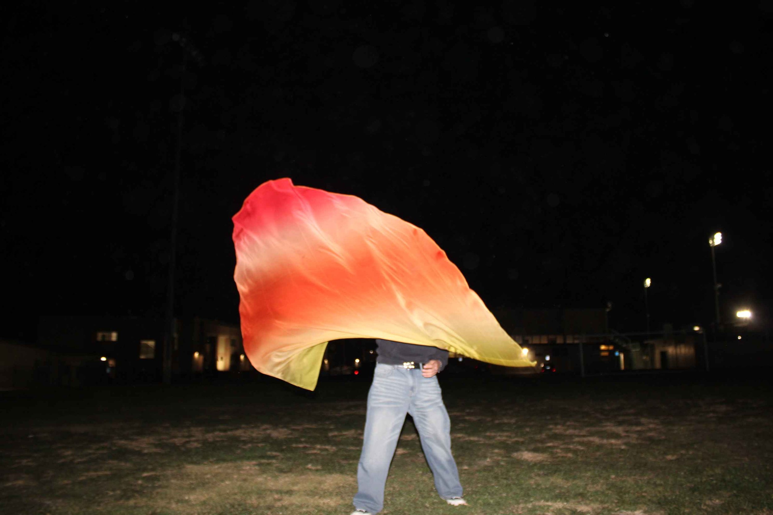 Person waving a large red and orange gradient flag outdoors at night