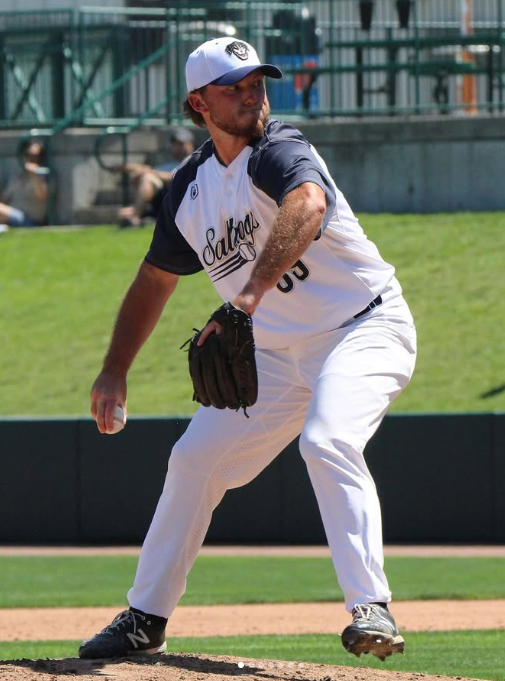 A baseball player in a white and navy uniform with a cap, preparing to pitch on the mound during a game.
