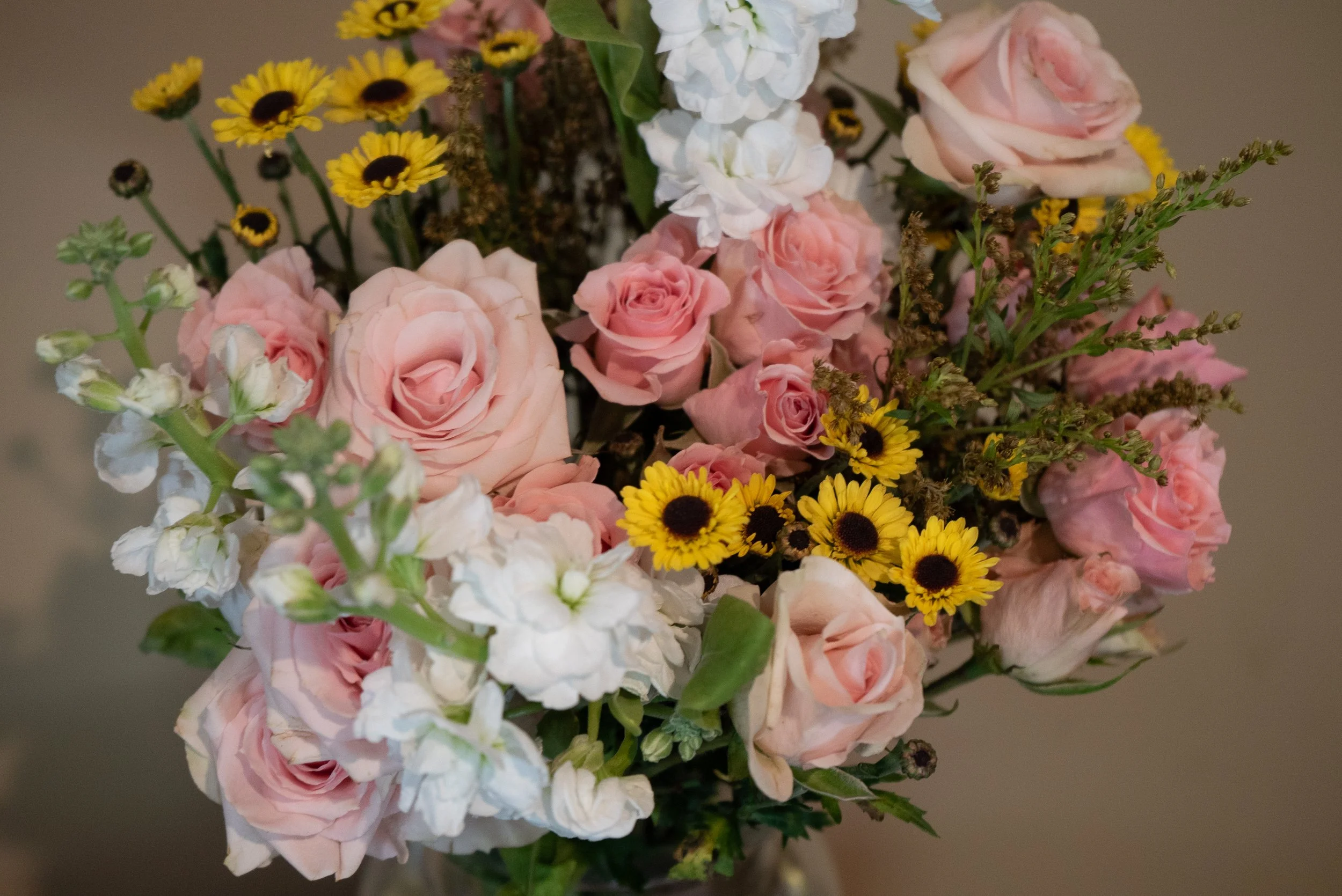 A bouquet of pink roses, yellow daisies, and white flowers arranged with green foliage.