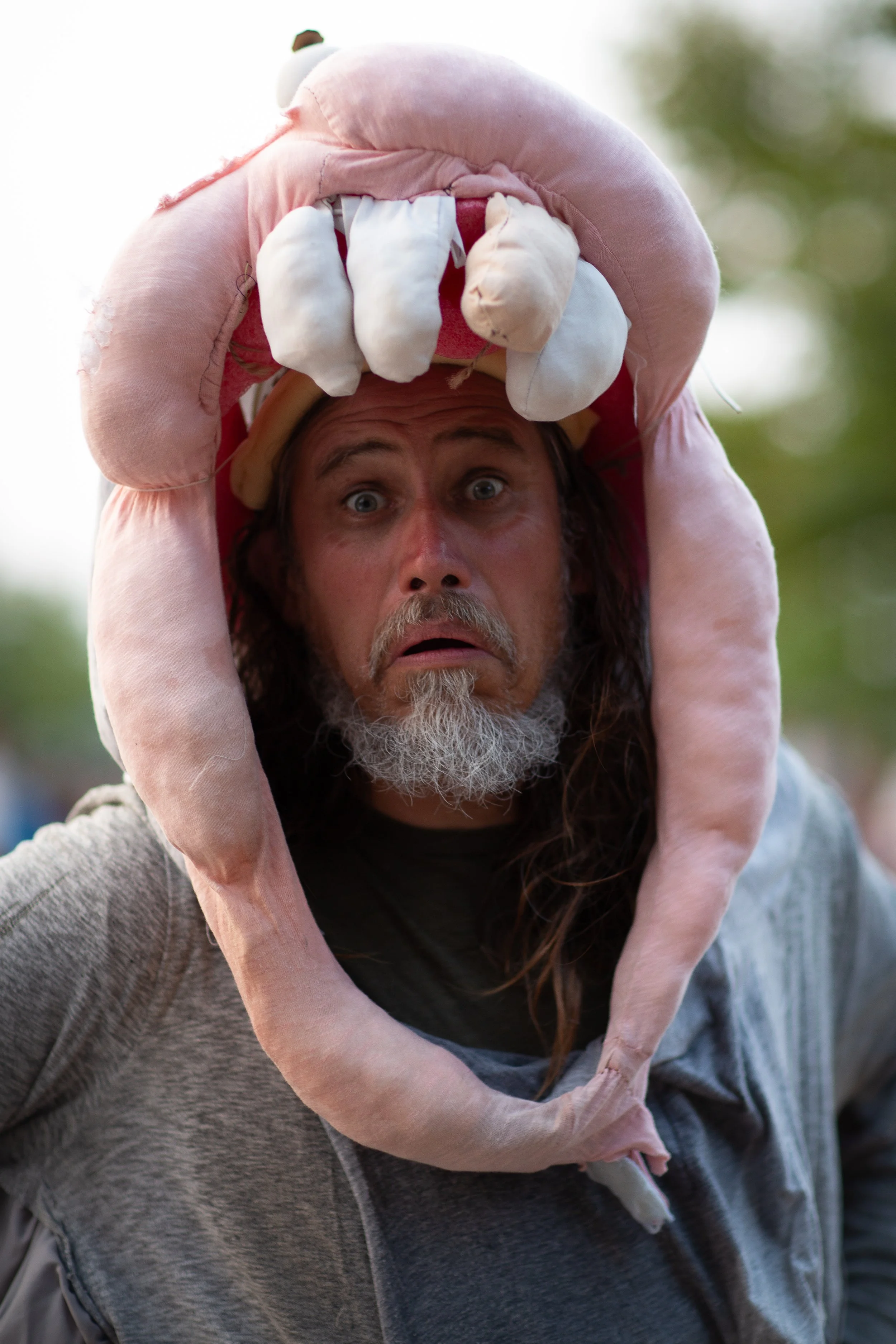 A man with long hair and a beard wearing a pink animal costume hat with a surprised expression.