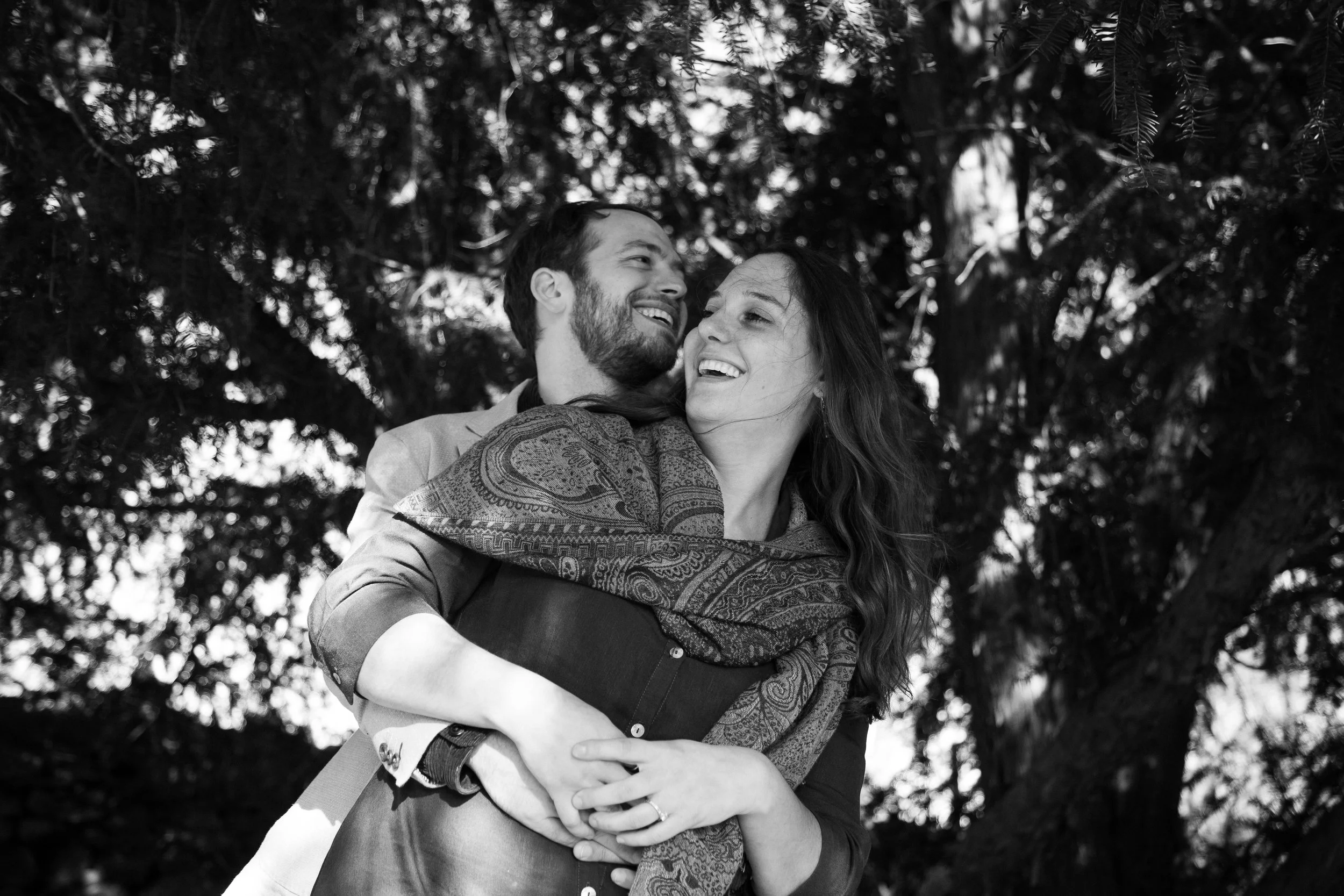 A happy couple, a man and a woman, sharing a joyful embrace outdoors with trees in the background, in black and white.