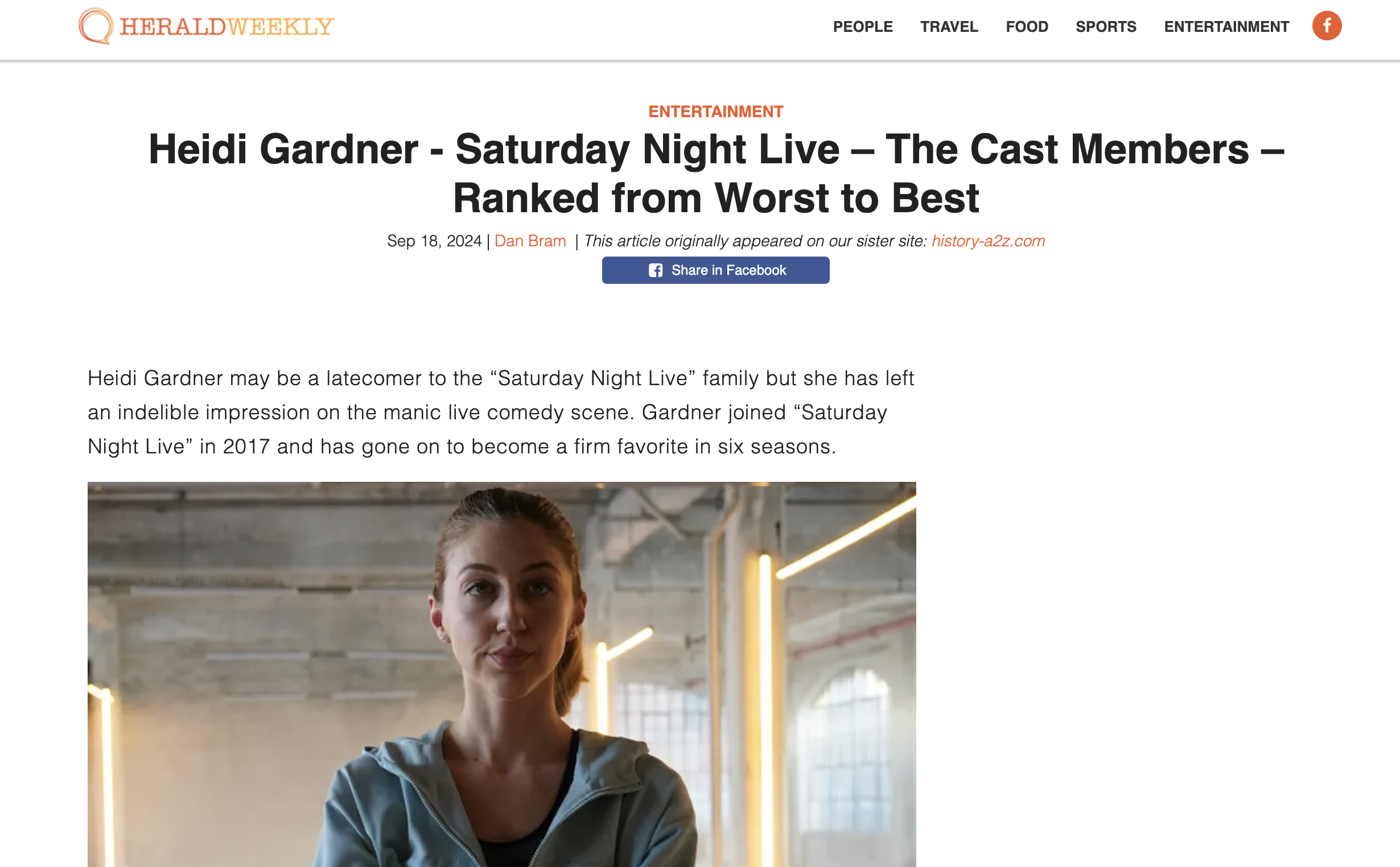 A woman with brown hair tied back, wearing a light blue jacket, standing indoors with a neutral expression. The background shows an industrial-style space with exposed pipes, concrete walls, and warm lighting.
