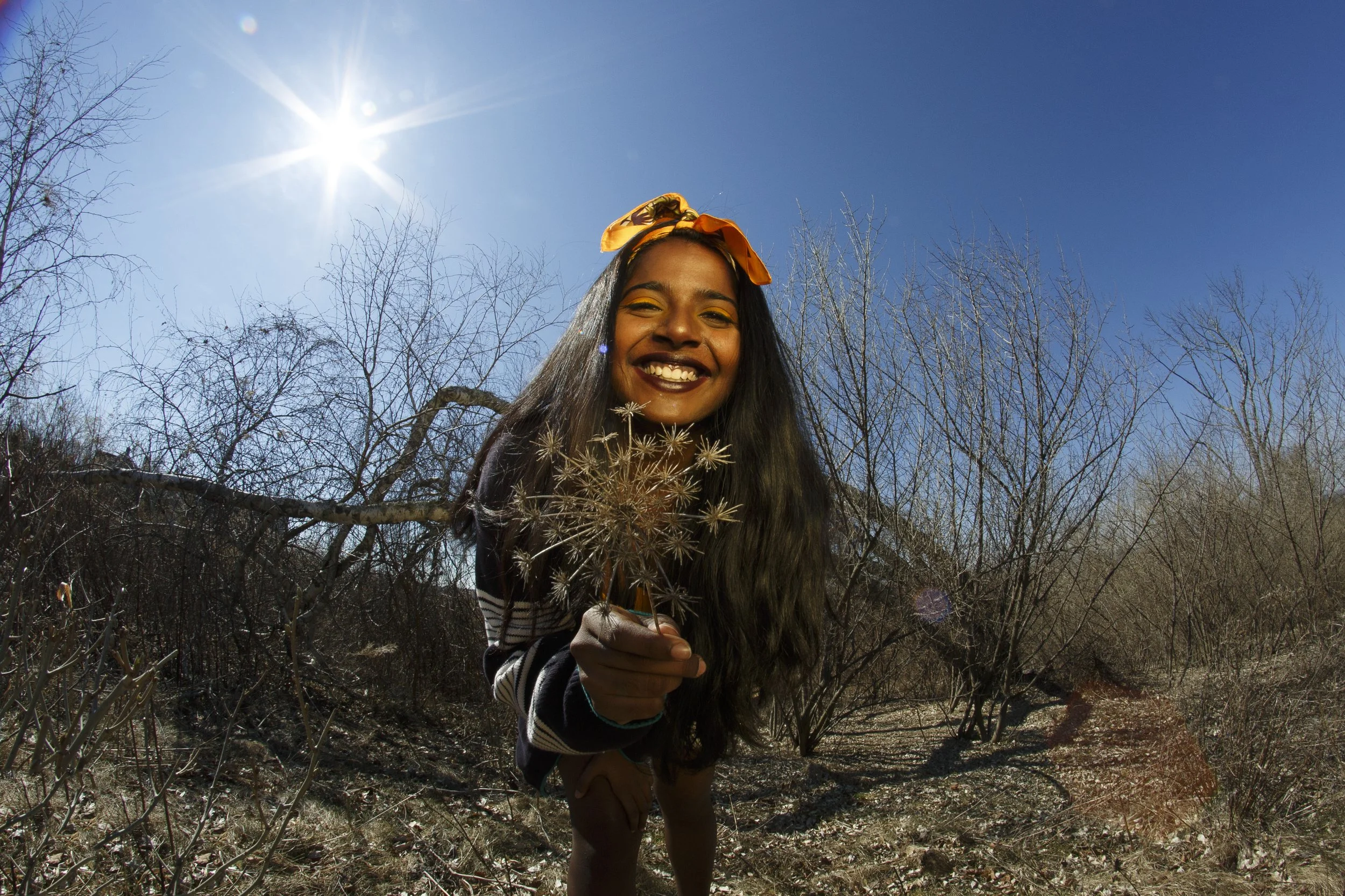 Young woman smiling and holding a dandelion in a dry, leafless forest on a sunny day.