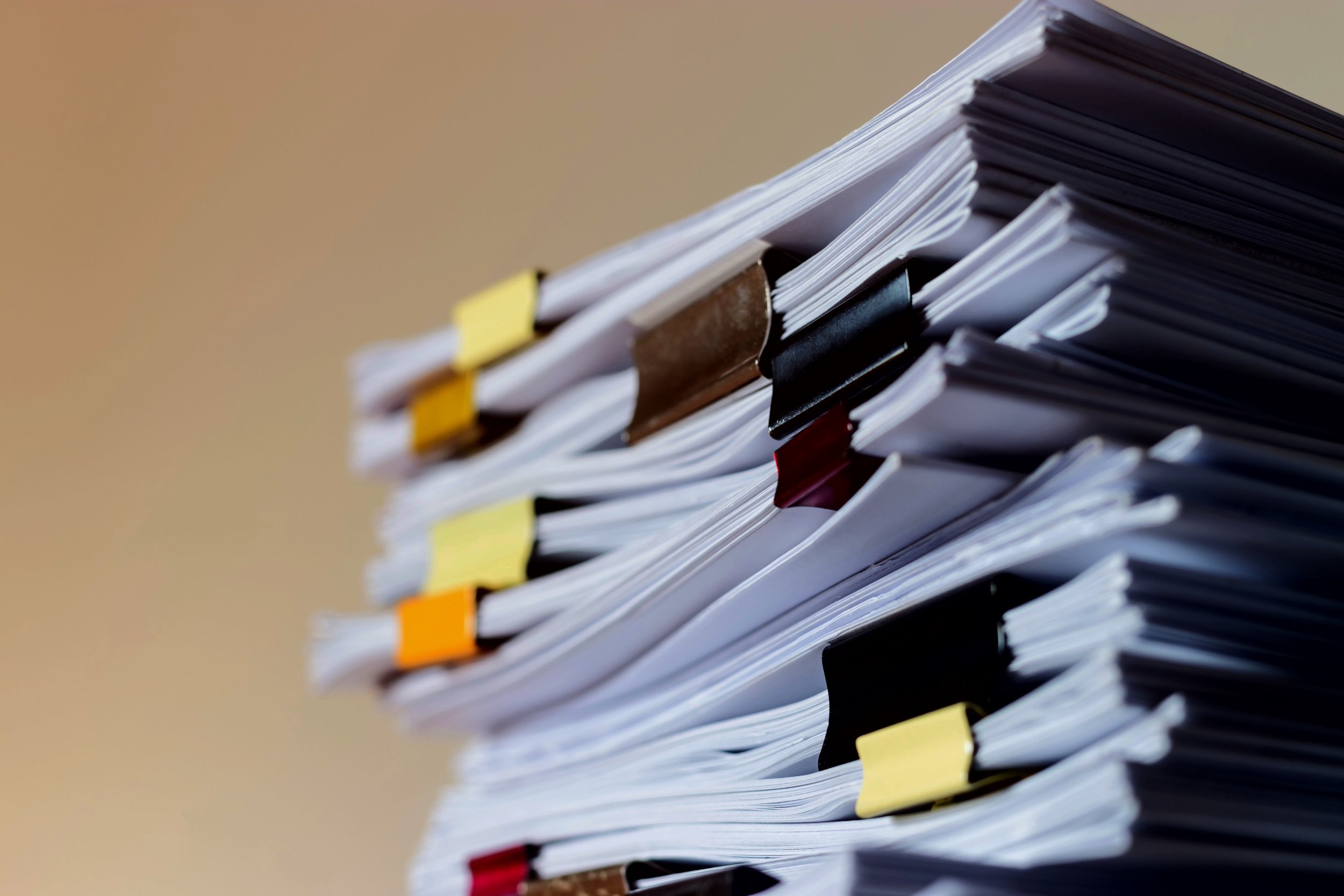 A large stack of paperwork with colorful tabs in a corner or on a desk.