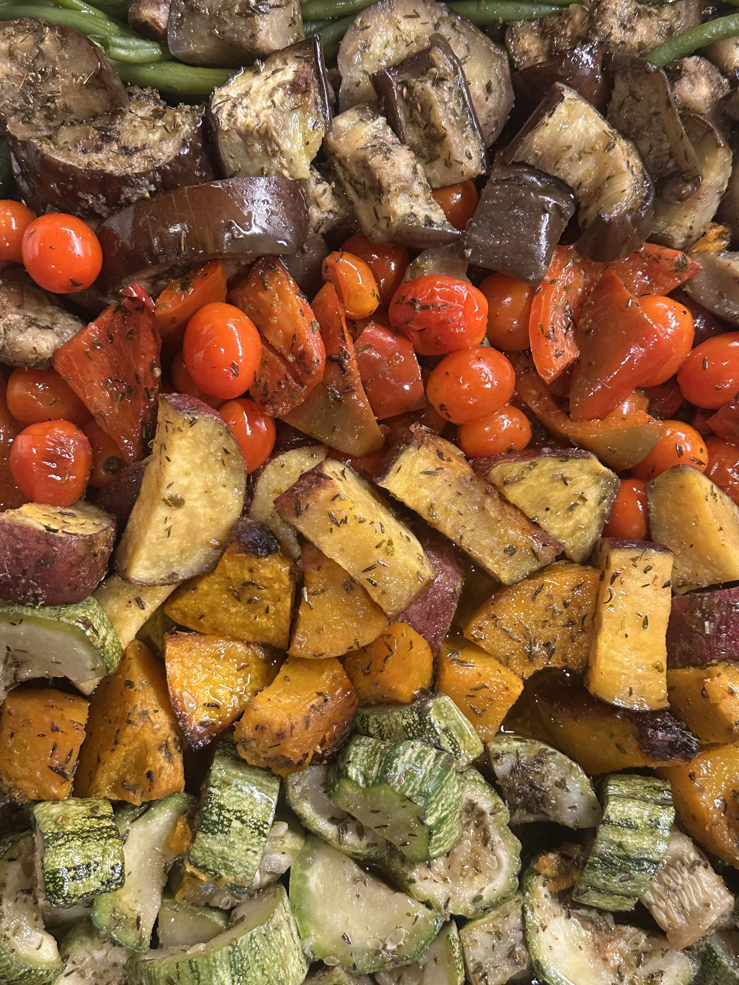 Close-up of roasted mixed vegetables, including eggplant, cherry tomatoes, zucchini, and sweet potatoes, garnished with herbs.