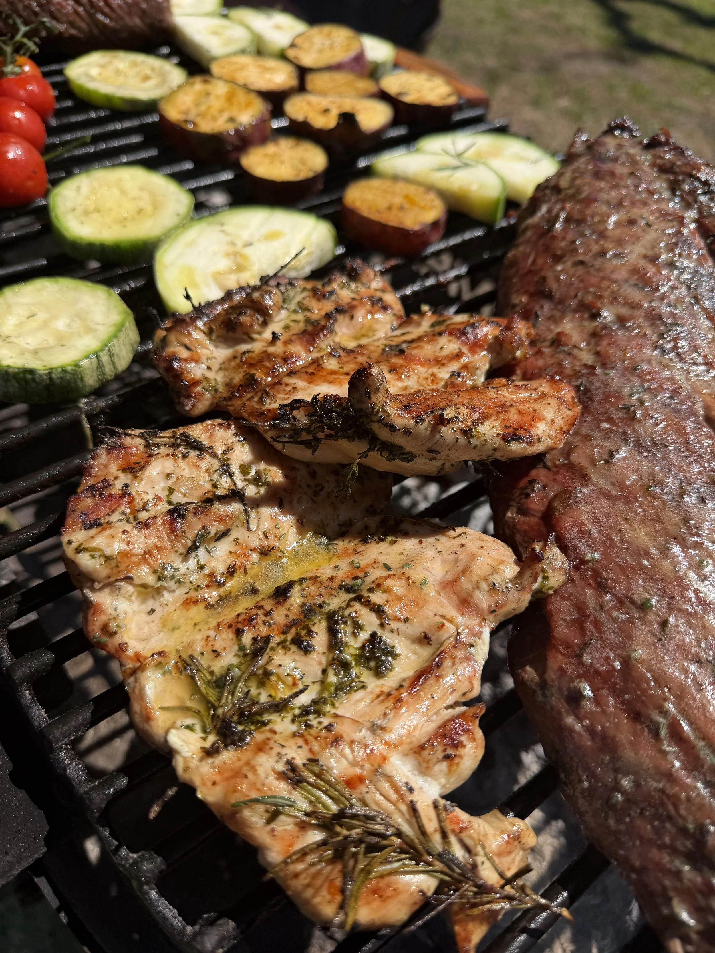 Barbecue grill with chicken breasts, shrimp, eggplant slices, zucchini slices, cherry tomatoes, and a sausage.