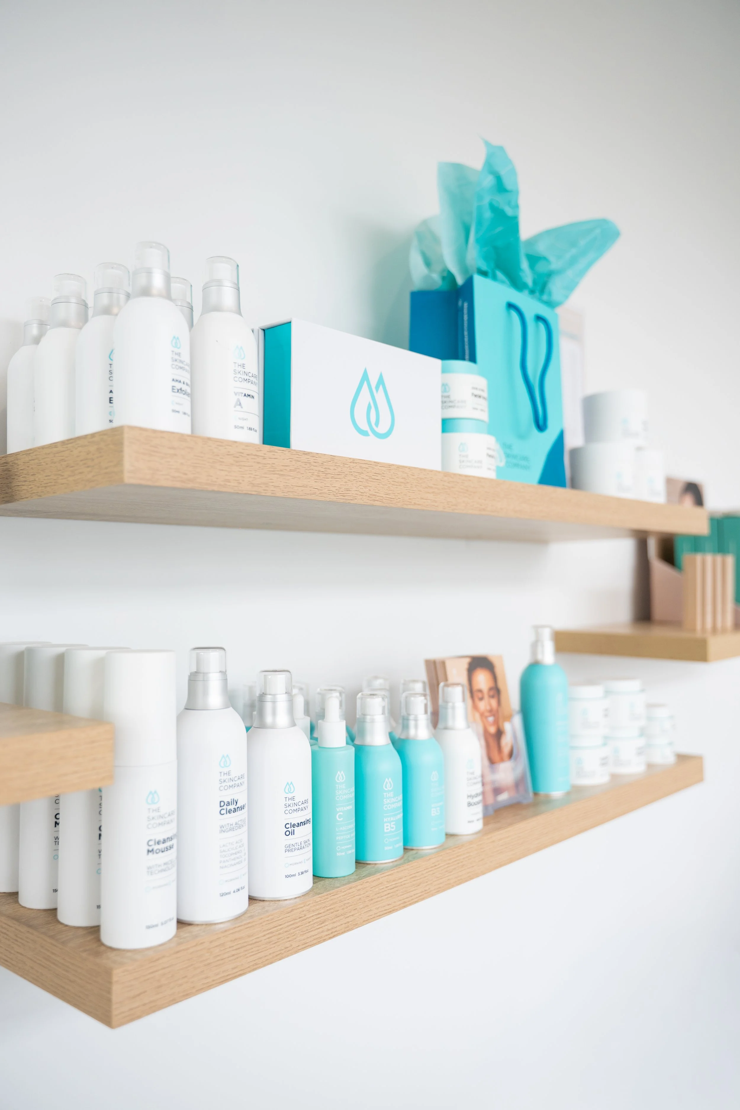 Wooden shelves with skincare products, including bottles and jars, arranged in rows, with a blue gift bag with tissues behind the products.
