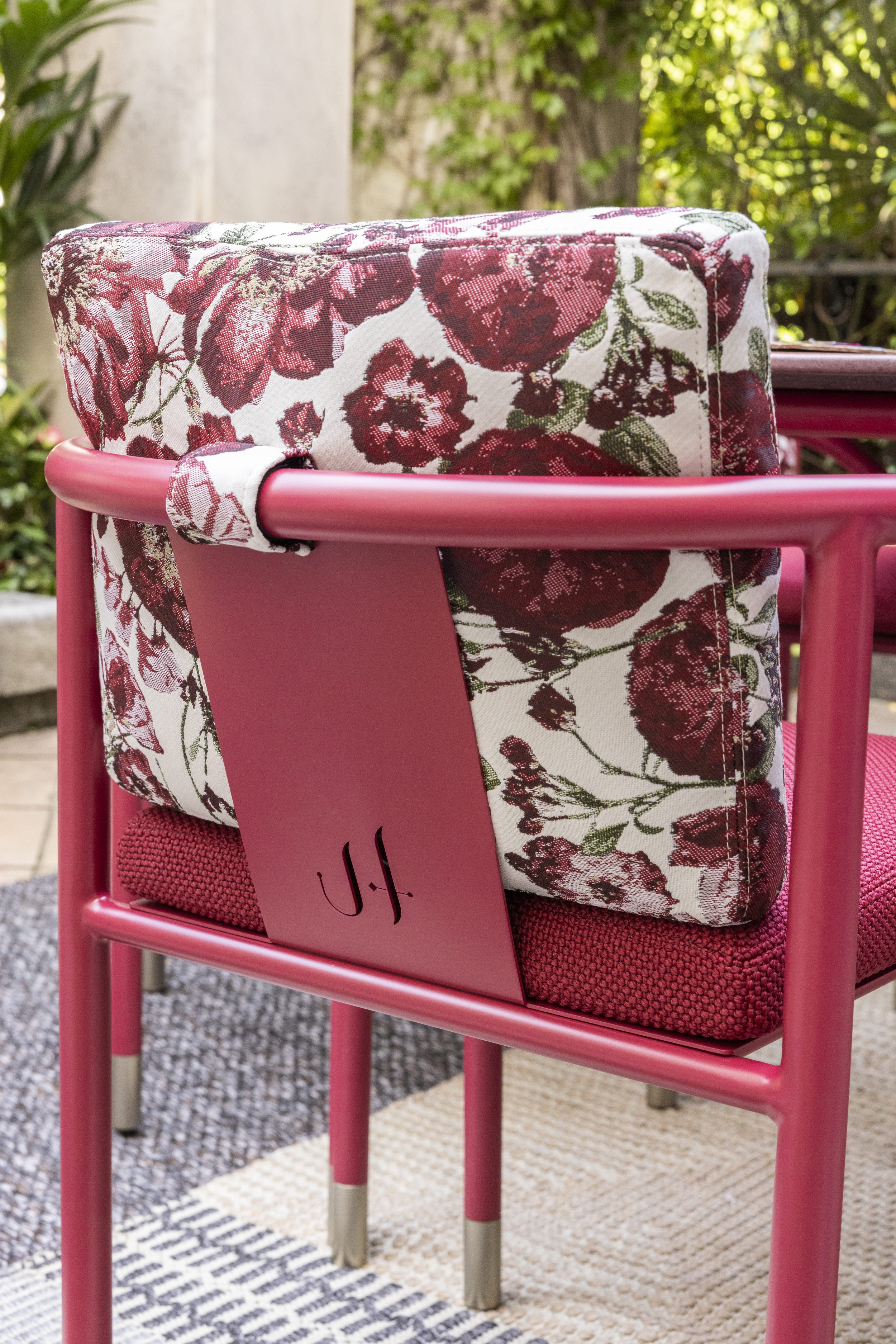 Sedie da esterno di colore rosa con cuscini a fiori rossi e bianchi e dettagli verdi e un numero '41' appeso alla sedia.