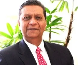 Person in a suit with a red tie, standing in front of a plant.