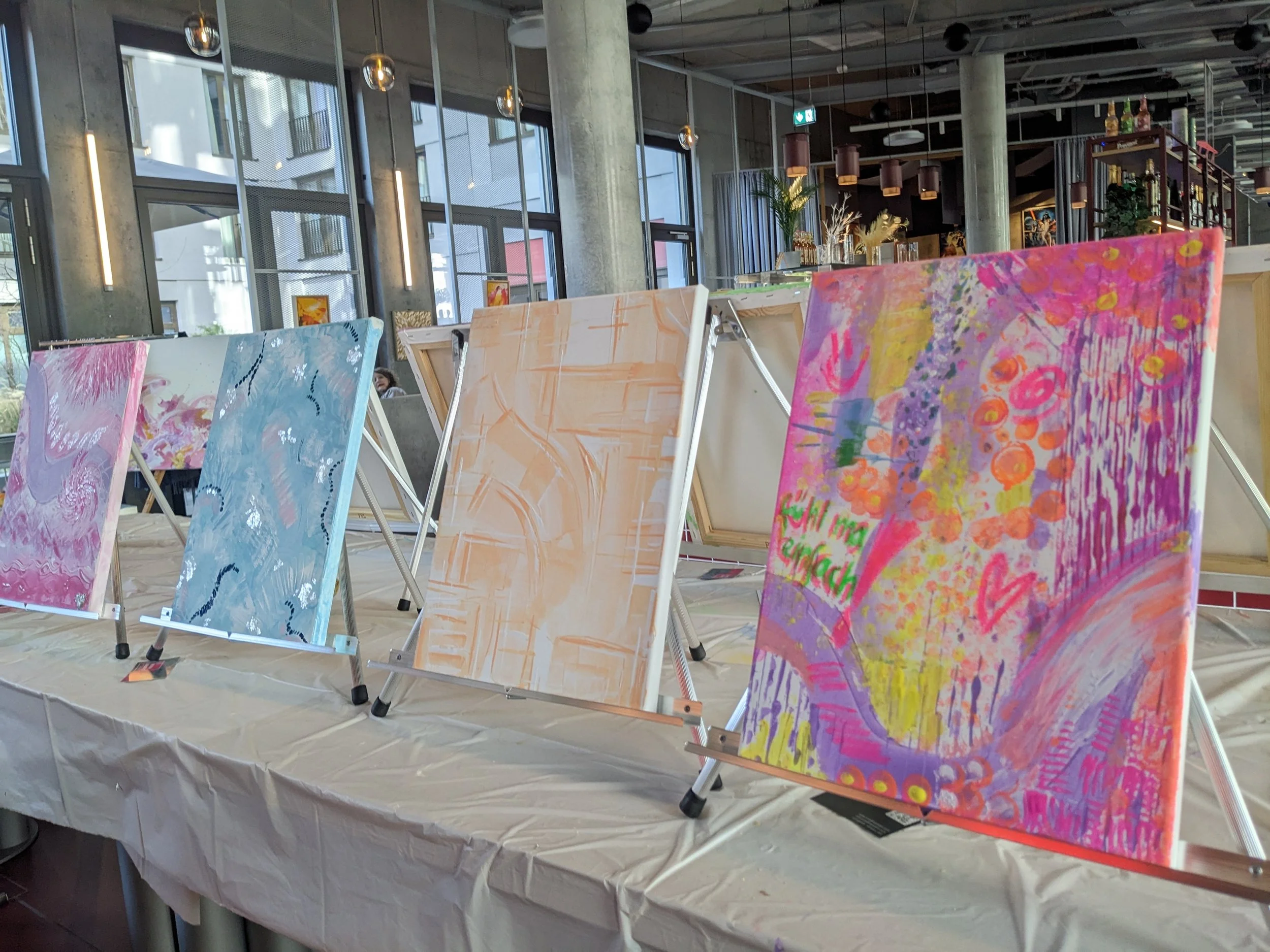 Bunte, abstrakte Gemälde auf Staffeleien in einem modernen, lichtdurchfluteten Raum.