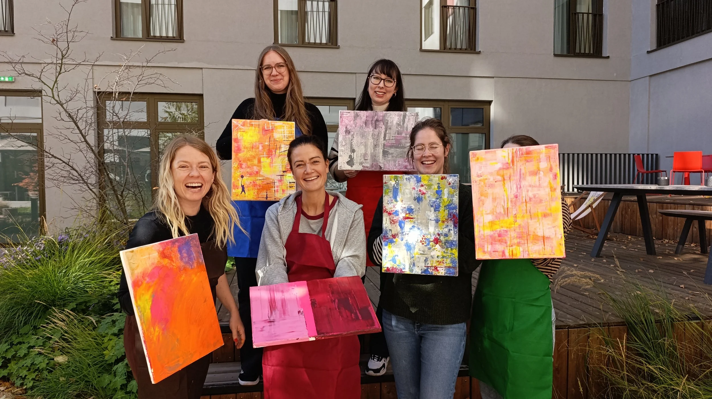Gruppenfoto von sechs Frauen, die im Freien mit ihren Kunstwerken lachen und posieren.