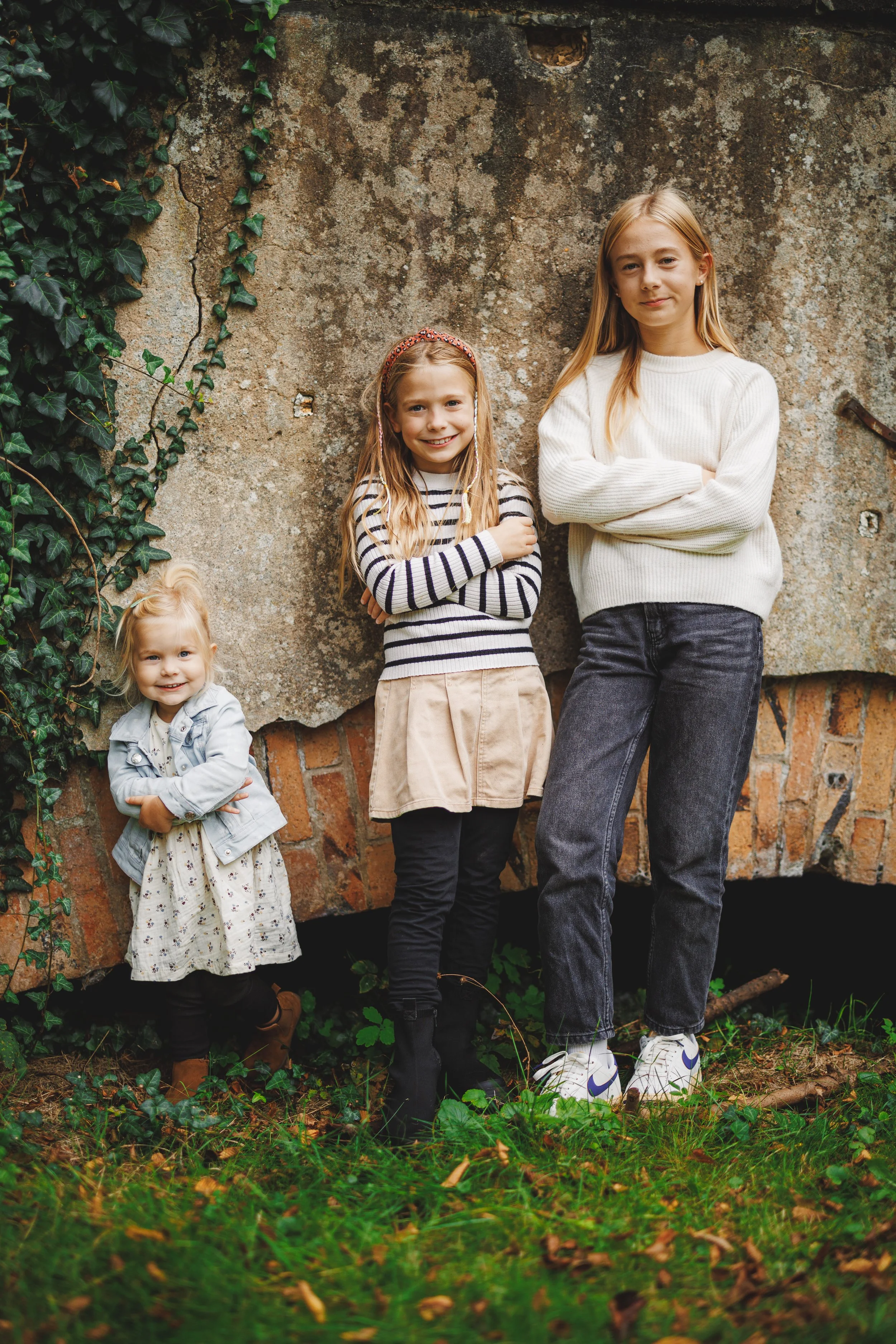 Geschwisterfoto beim Mini-Shooting: drei Mädchen stehen draußen vor einer Wand und schauen entspannt in die Kamera.