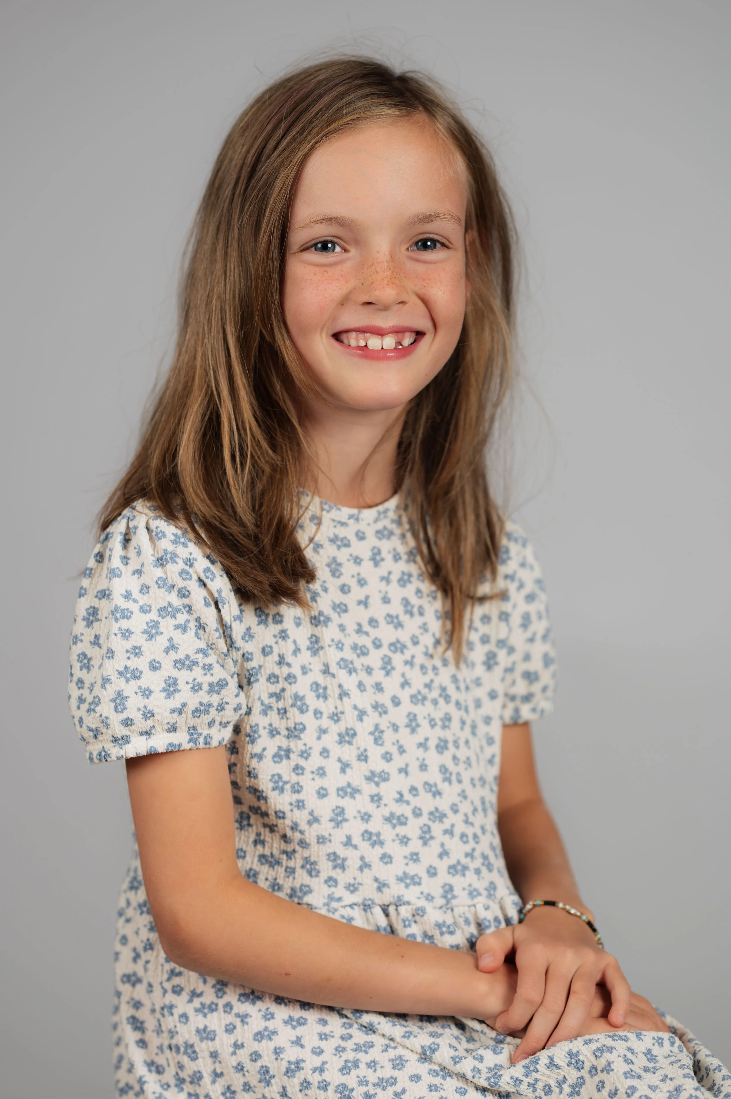 Schulfotografie im Studio mit neutralem grauem Hintergrund. Natürliches Licht, entspannte Haltung und ein ehrliches Porträt, das Persönlichkeit in den Mittelpunkt stellt.