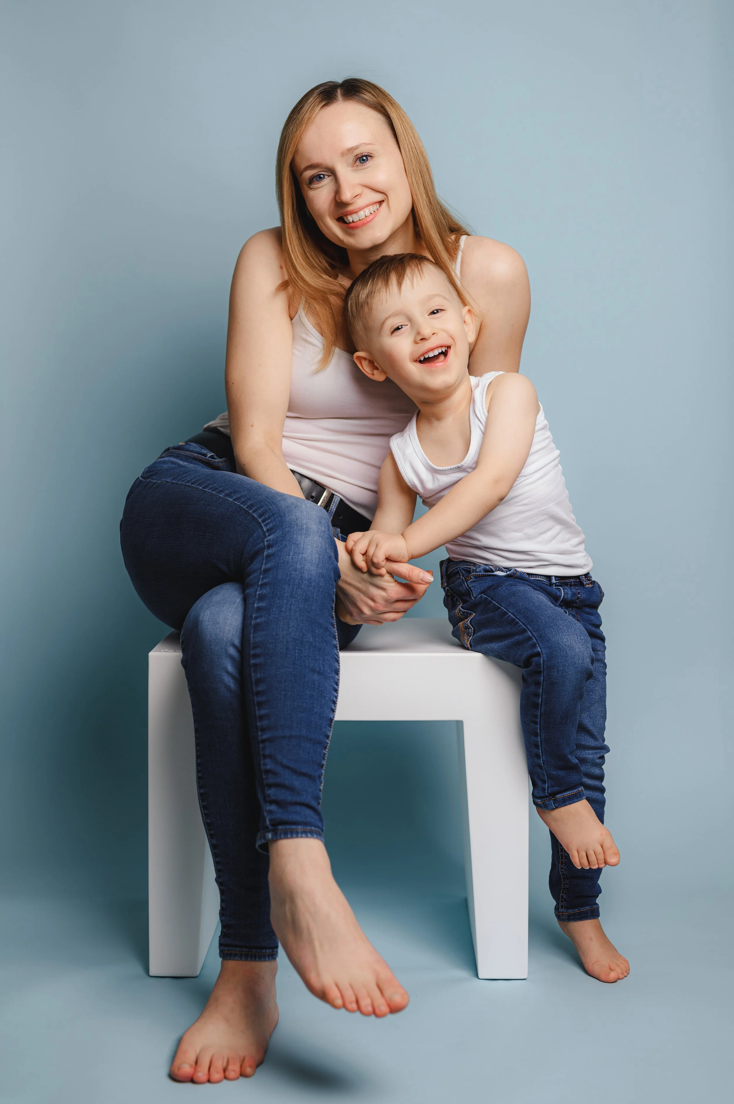 Natürliches Eltern-Kind-Foto aus der Kita-Fotografie: Ein Elternteil und ein Kind sitzen entspannt zusammen auf einem Hocker vor blauem Hintergrund. Das Bild zeigt Nähe, Vertrauen und einen ruhigen Moment im Rahmen eines Kita-Fototags.