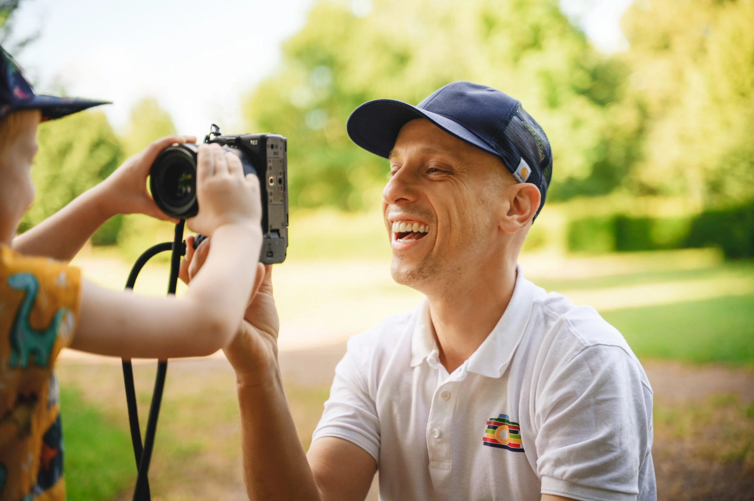 Ein Kind fotografiert den lachenden Kita-Fotografen Ron Marzok bei einer spielerischen Begegnung im Freien.