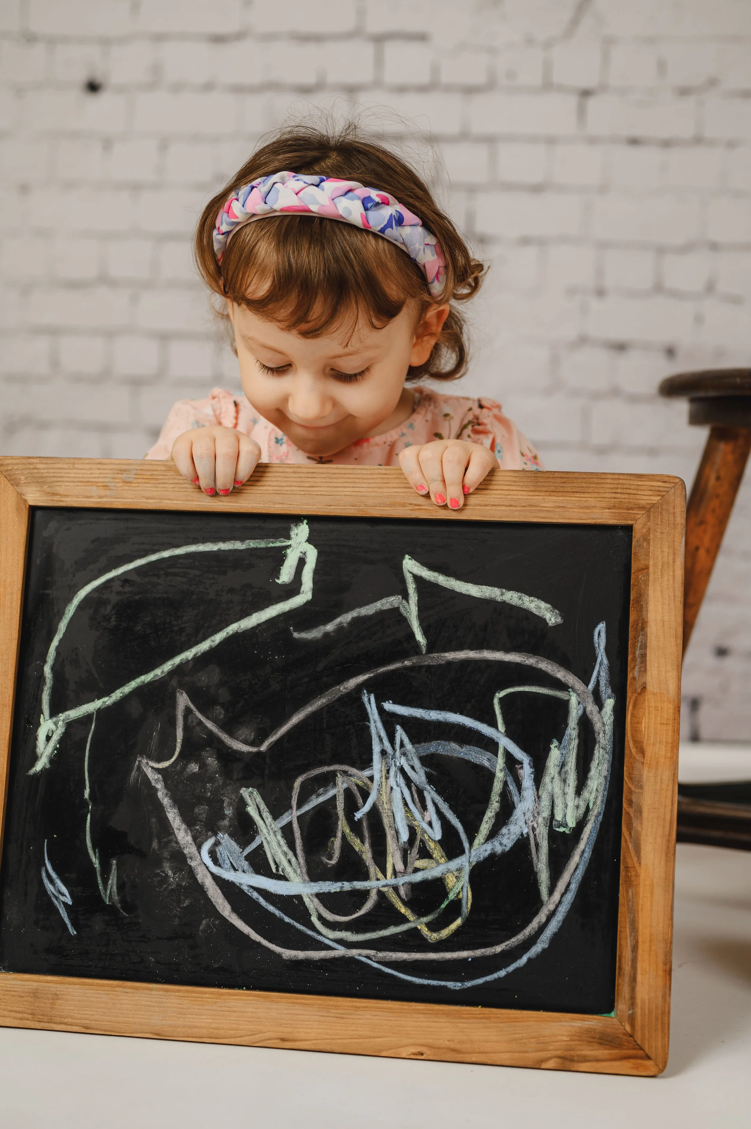 Ein Kind präsentiert stolz sein selbst gemaltes Kunstwerk auf einer Kreidetafel.
Bunte Kreidestriche, konzentrierter Blick und eine ruhige Studioatmosphäre schaffen ein authentisches, kreatives Porträt.
Das Kreidetafel-Set lädt Kinder dazu ein, sich 