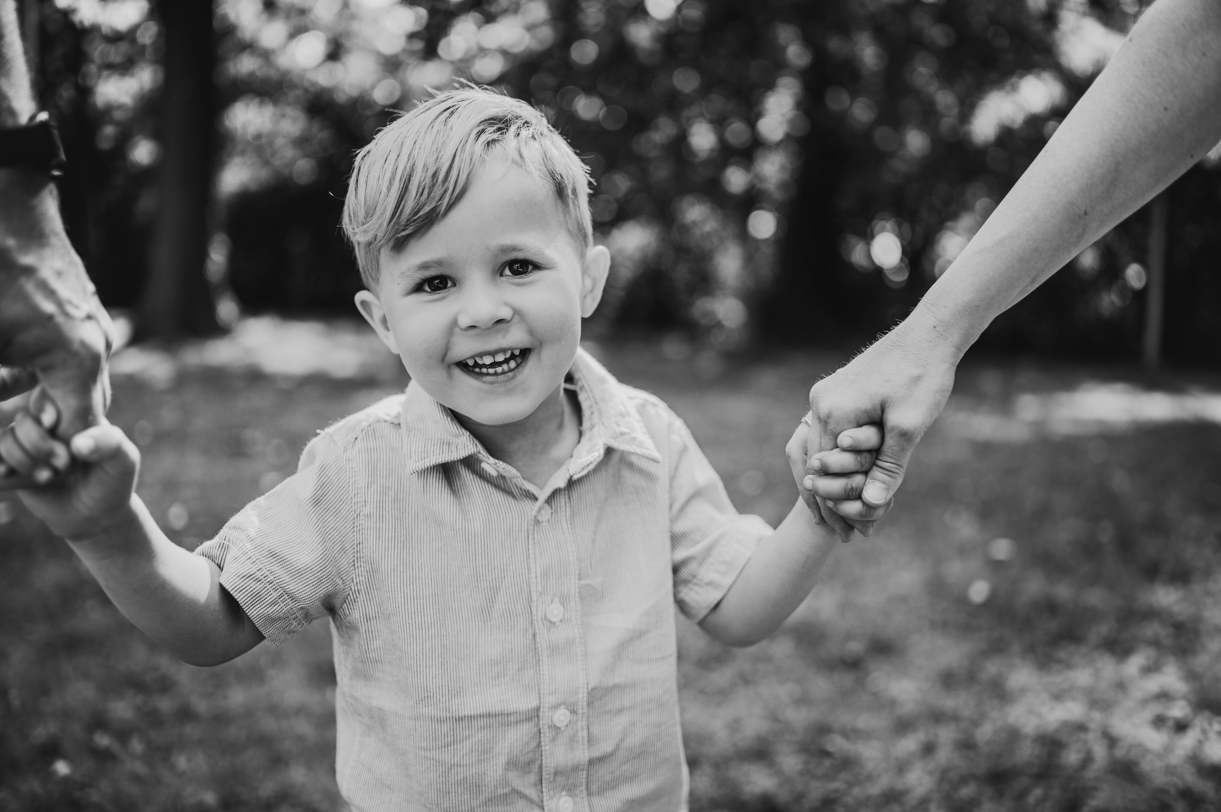 Schwarzweißfoto eines lachenden Kindes, das die Hände der Eltern hält – natürlicher Mini Shooting Moment in Südbrandenburg und Sachsen.