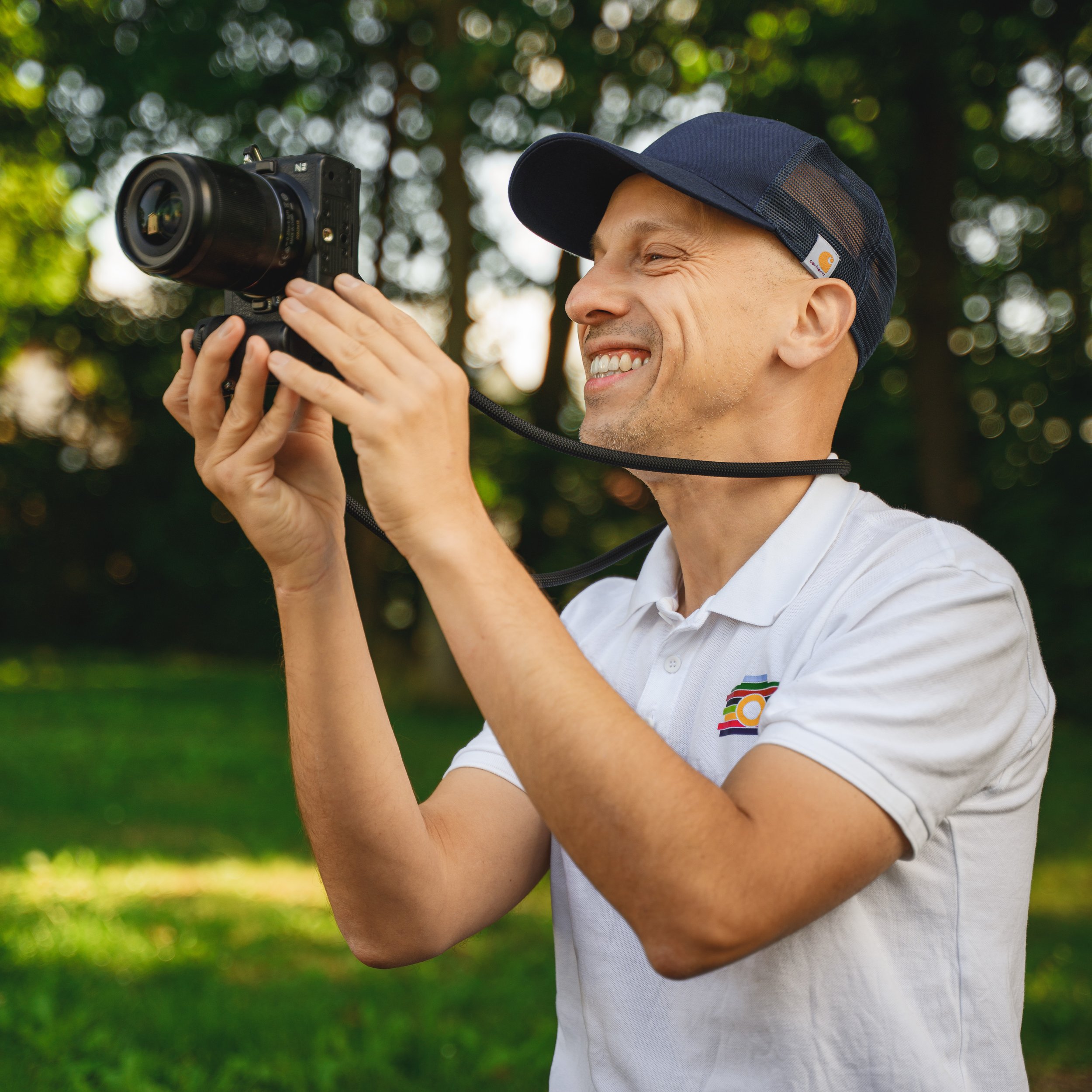 Kita-Fotograf Ron Marzok lächelt mit seiner Kamera bei einem Fotoshooting im Grünen.