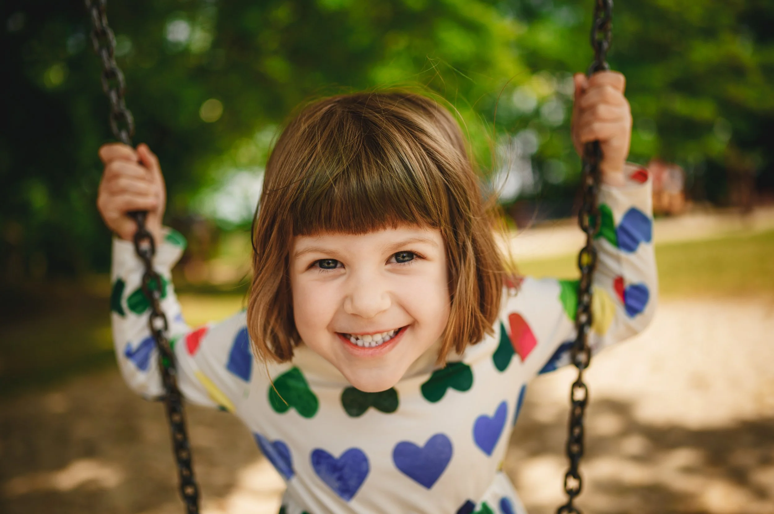 Ein lachendes Kita-Kind schaukelt im Garten und blickt direkt in die Kamera. Authentische Outdoor-Kita-Fotografie mit natürlichem Licht und spielerischer Leichtigkeit.