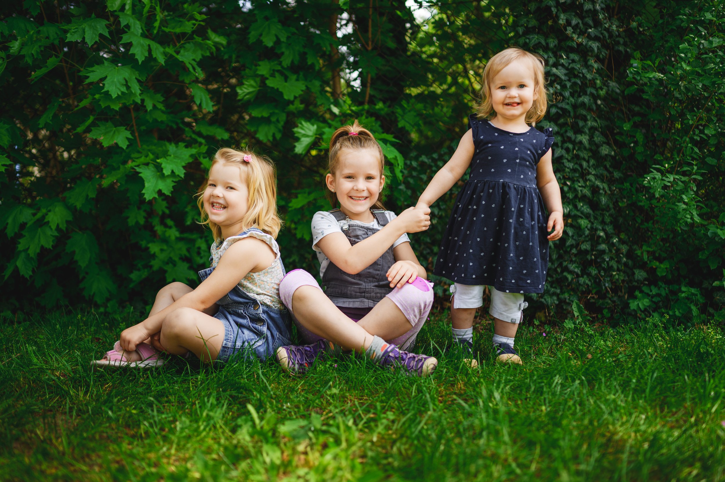Drei Kinder sitzen und stehen lachend im Grünen – natürliches Geschwisterfoto bei einem Mini Shooting in Südbrandenburg und Sachsen.
