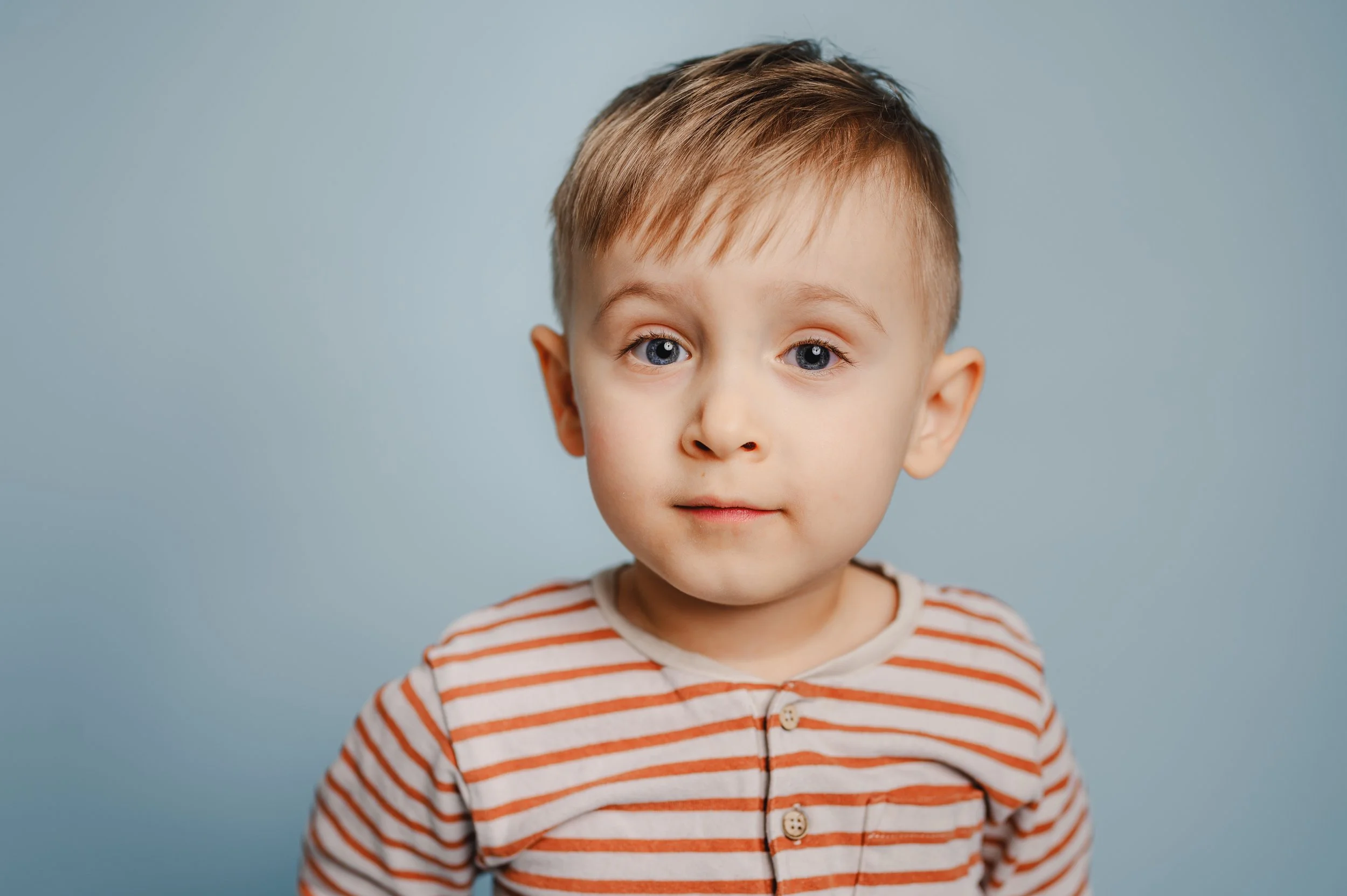 Natürliches Porträt eines Kindes vor blauem Hintergrund. Der ruhige Bildaufbau und der sanfte Ausdruck stehen für moderne, einfühlsame Kita-Fotografie mit Fokus auf echte Momente.