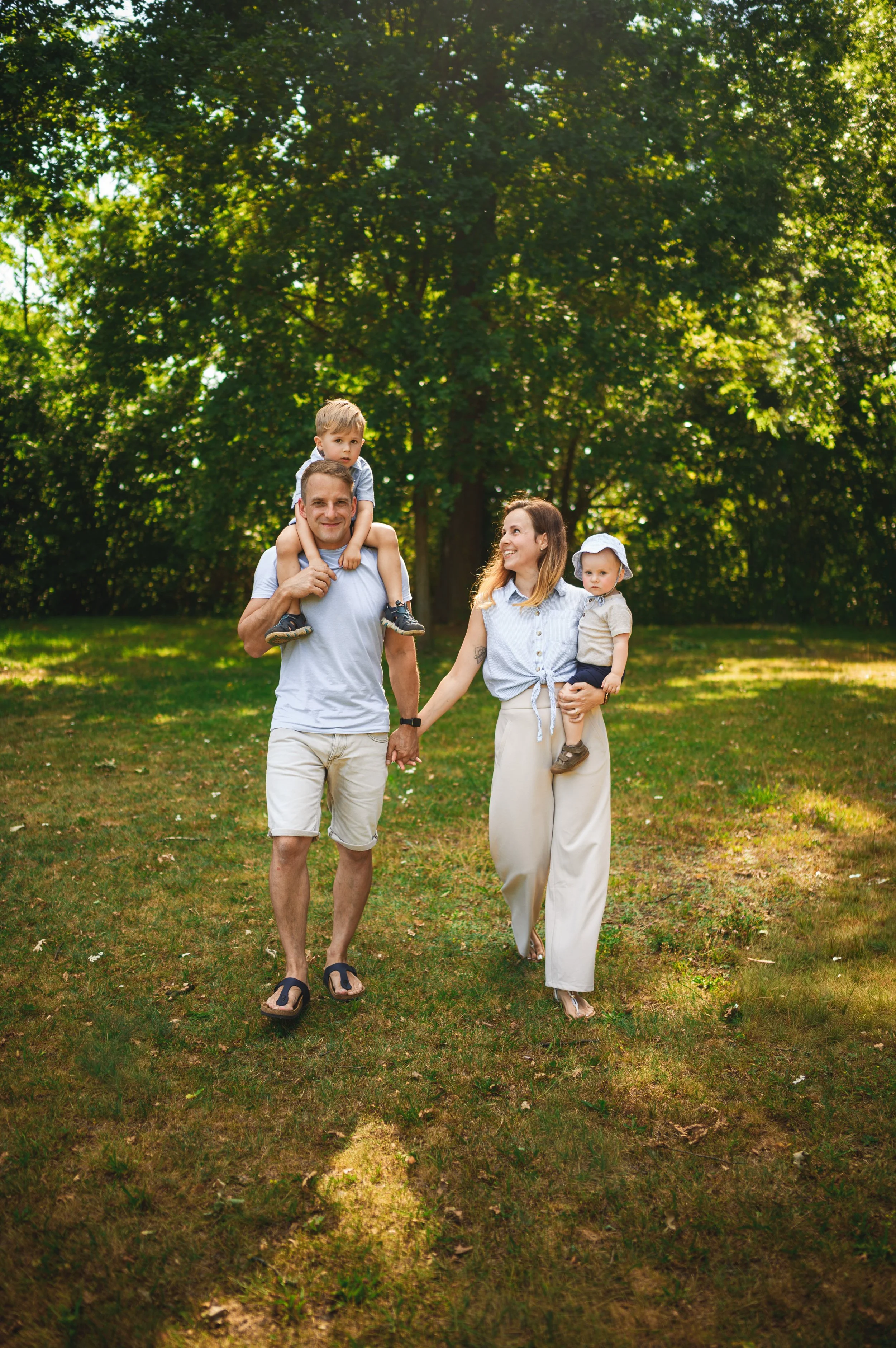 Familie mit zwei kleinen Kindern spaziert im Park unter Bäumen – natürliche Mini Shooting Aufnahme für Familien in Südbrandenburg und Sachsen.