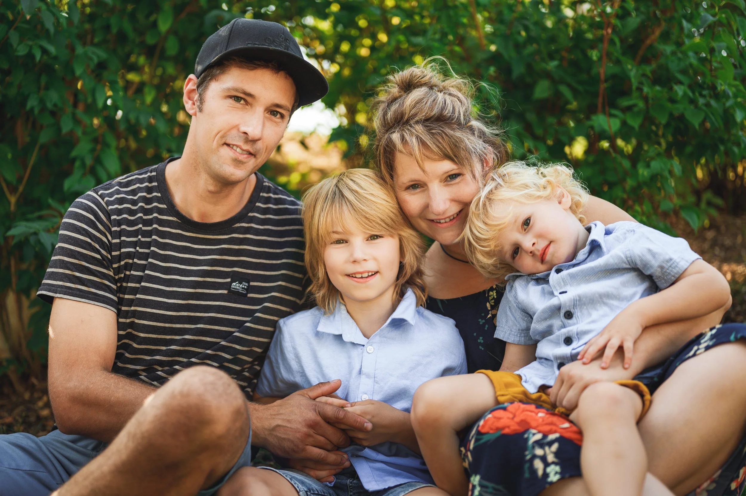 Familie mit zwei Kindern sitzt nah beieinander im Grünen – natürliches Familienfoto bei einem Mini Shooting in Südbrandenburg und Sachsen.