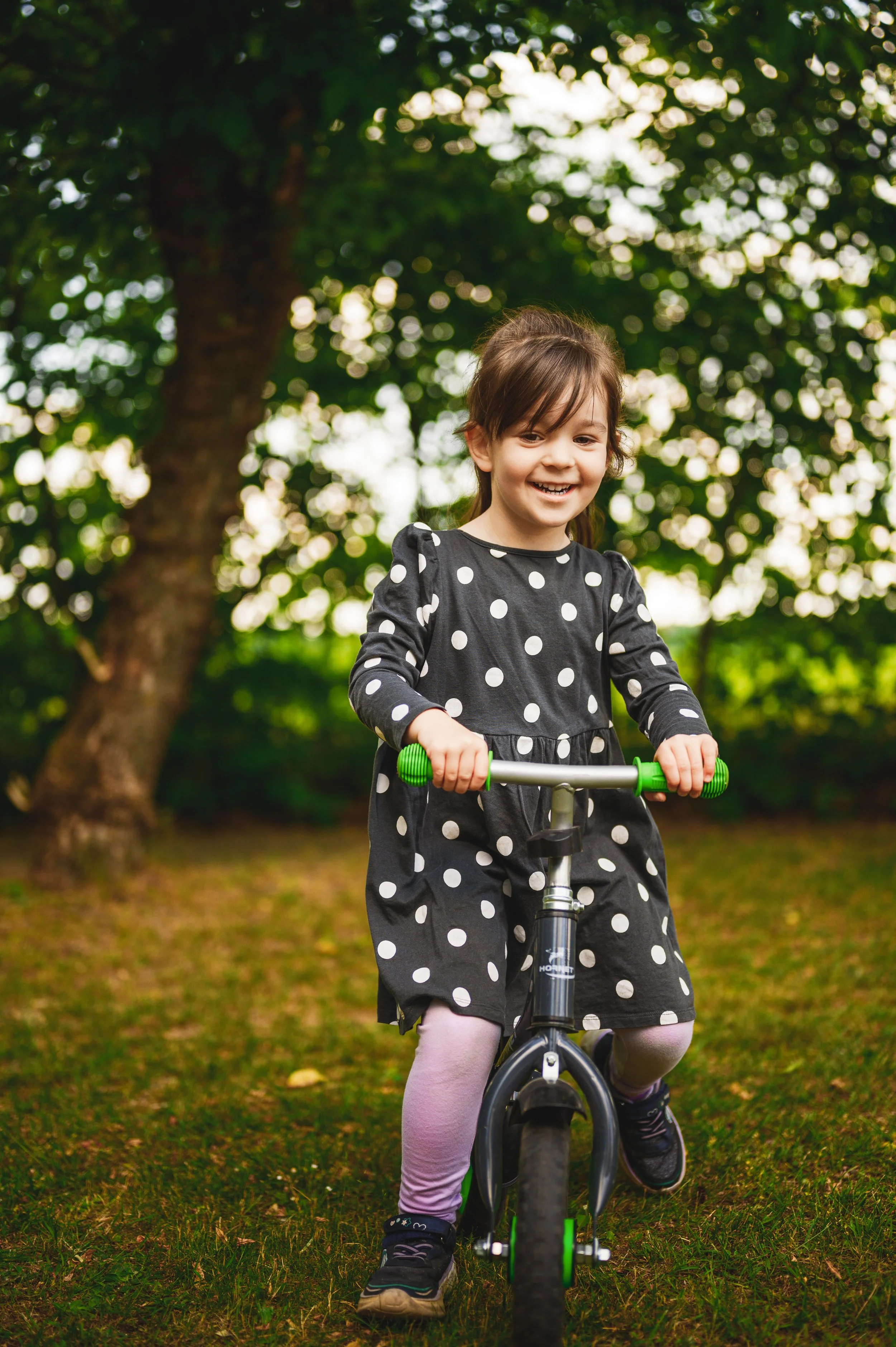 Fröhliches Kind fährt mit dem Laufrad im grünen Kita-Außenbereich – natürliche und authentische Kita-Fotografie von KUNTERBUNTE MOMENTE.