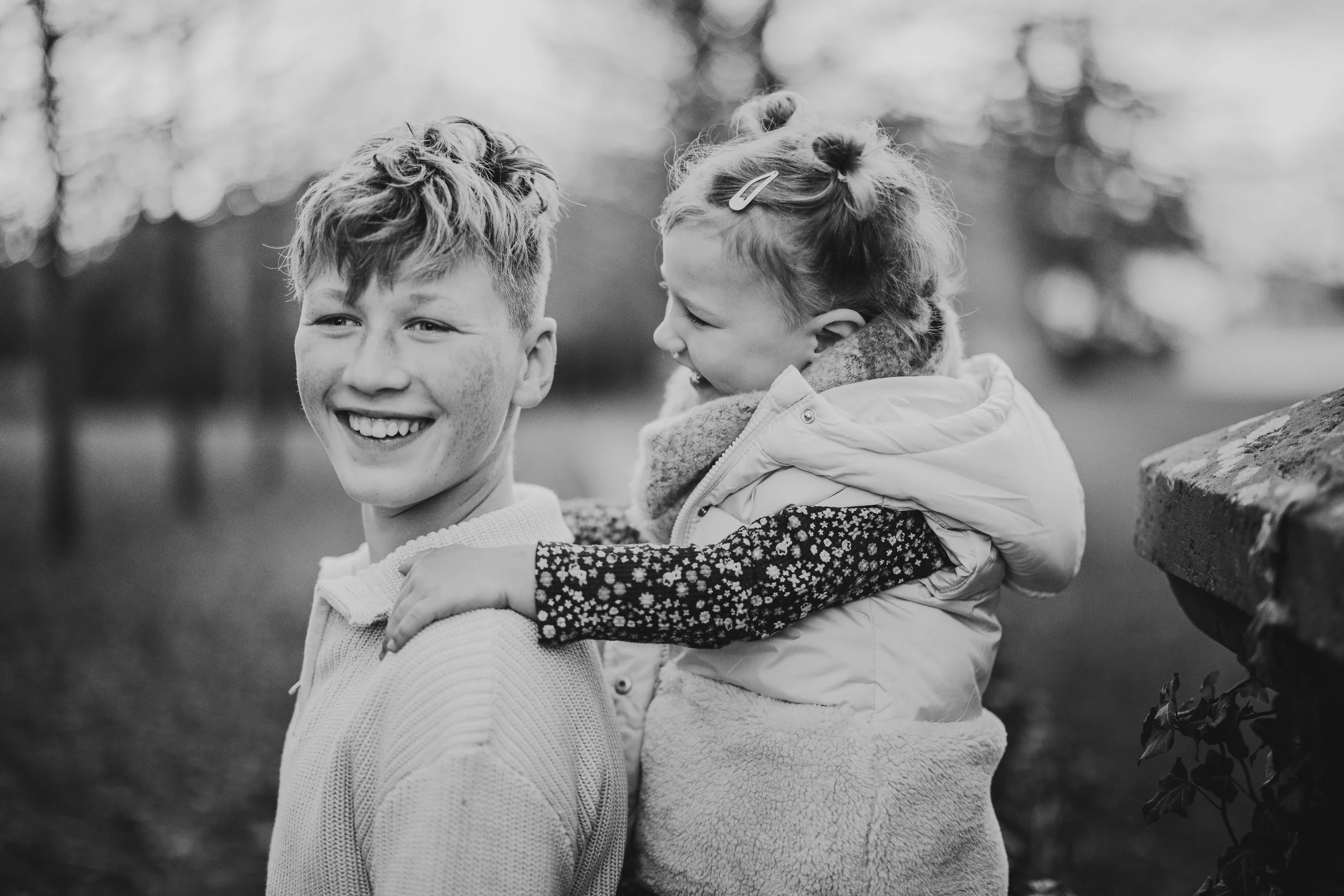 Schwarzweißfoto von Geschwistern: ein Junge trägt ein jüngeres Kind auf dem Rücken – natürlicher Mini Shooting Moment in Südbrandenburg und Sachsen.