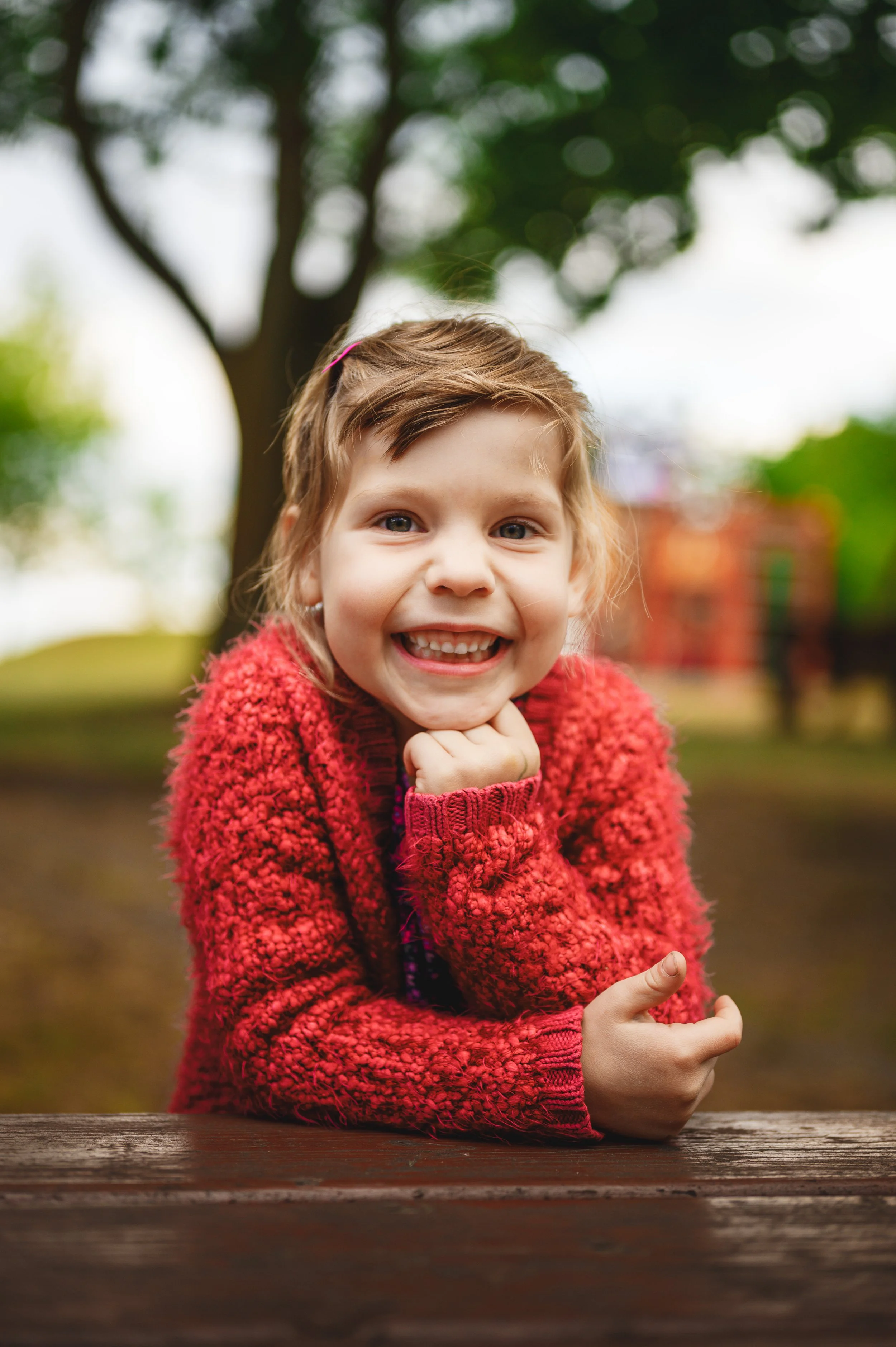 Natürliches Outdoor-Porträt eines Kita-Kindes in entspannter Haltung. Weiches Tageslicht, ruhiger Hintergrund und ein ehrliches, offenes Lächeln sorgen für eine warme und vertrauensvolle Bildwirkung. Moderne Kita-Fotografie ohne Zwang, kindgerecht un