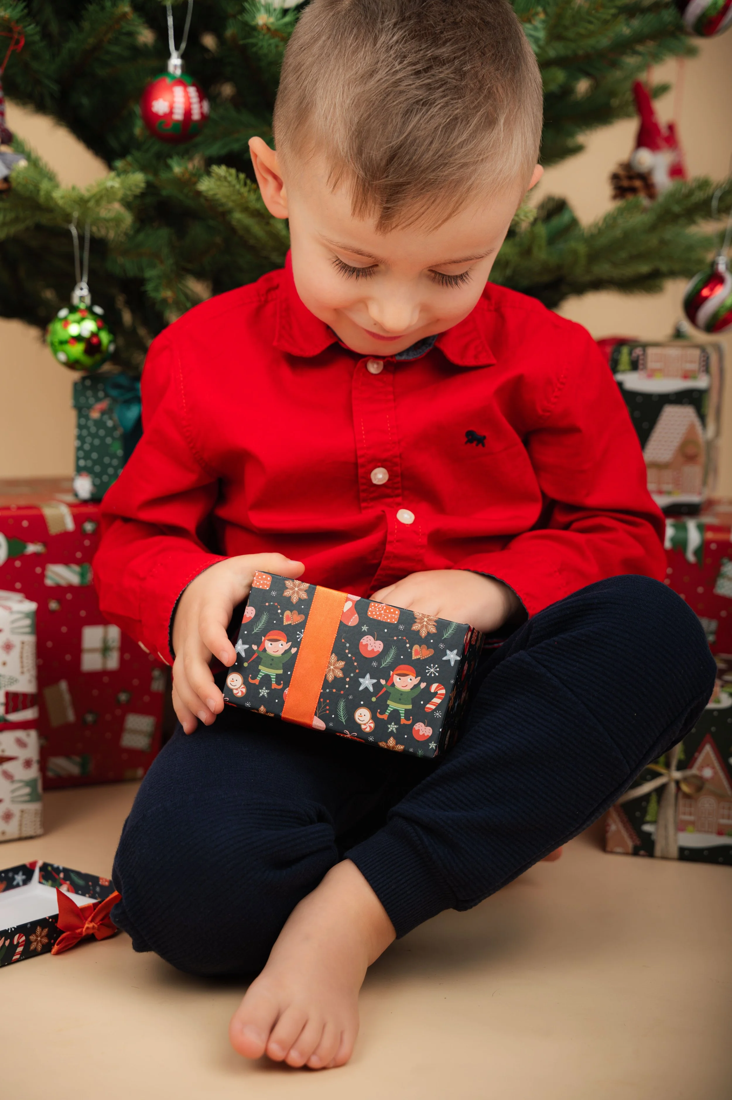 Weihnachtliches Kinderfoto im Studio: Ein Kind sitzt vor dem geschmückten Weihnachtsbaum und hält neugierig ein Geschenk in den Händen.
Warme Farben, ruhige Bildsprache und natürliche Momente machen dieses Foto zu einer zeitlosen Erinnerung – moderne