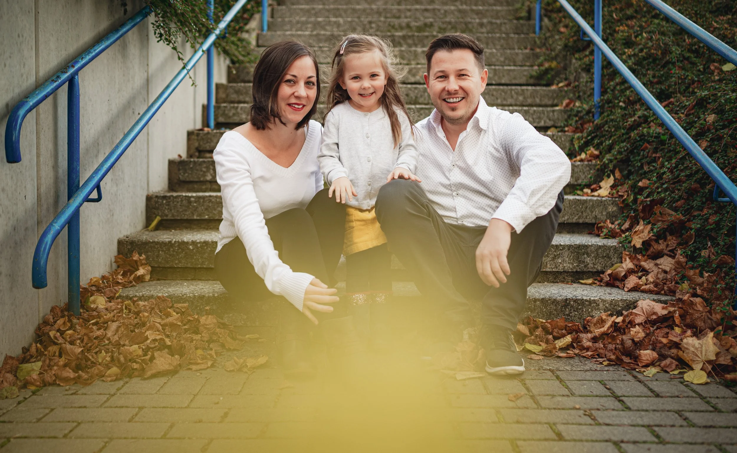 Familie mit Kind sitzt gemeinsam auf einer Treppe im Herbstlaub – natürliches Mini Shooting Familienfoto in Südbrandenburg und Sachsen.